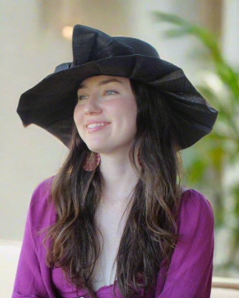 Model wearing Lilly 5" Brim Fan Straw Sun Hat with Big Bow Black handmade loomed natural raffia palm fiber in a solid hue of black with pleated wide brim and oversized bow embellishment - Shebobo