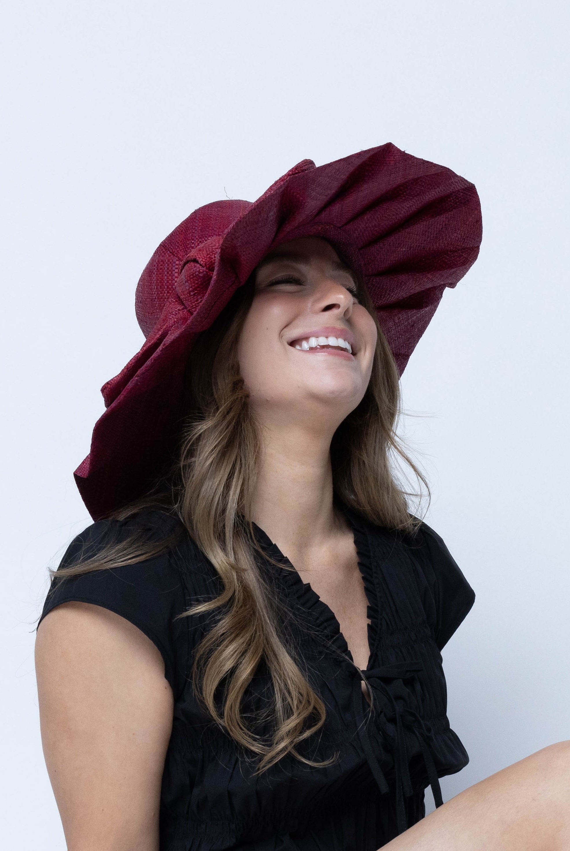 Model wearing Lilly 5" Brim Fan Straw Sun Hat with Big Bow Umberwine handmade loomed natural raffia palm fiber in a solid hue of umberwine bordeaux/claret/deep/dark/purple/red with pleated wide brim and oversized bow embellishment - Shebobo