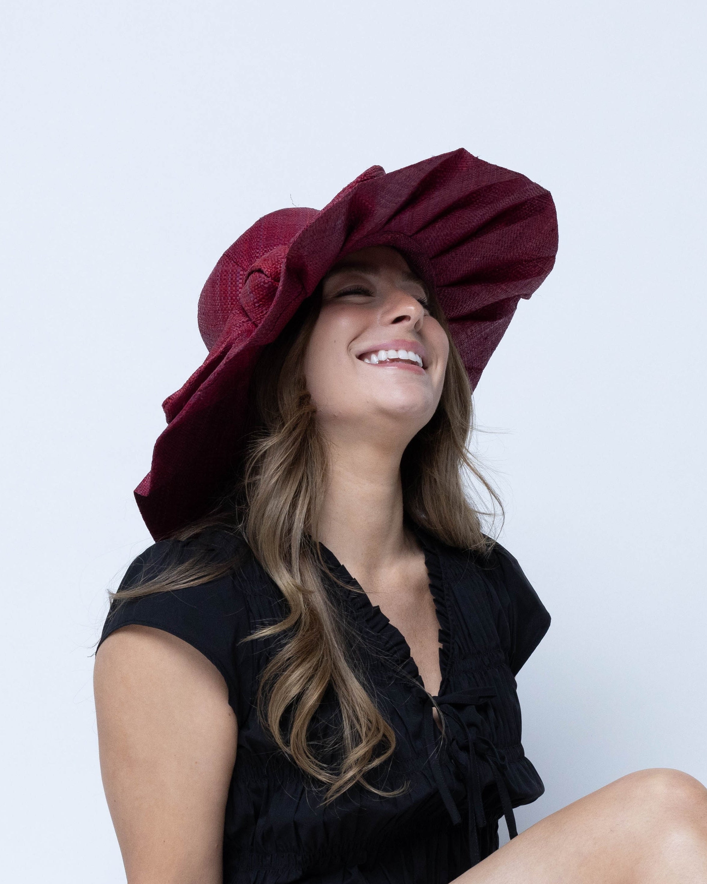 Model wearing Lilly 5" Brim Fan Straw Sun Hat with Big Bow Umberwine handmade loomed natural raffia palm fiber in a solid hue of umberwine bordeaux/claret/deep/dark/purple/red with pleated wide brim and oversized bow embellishment - Shebobo
