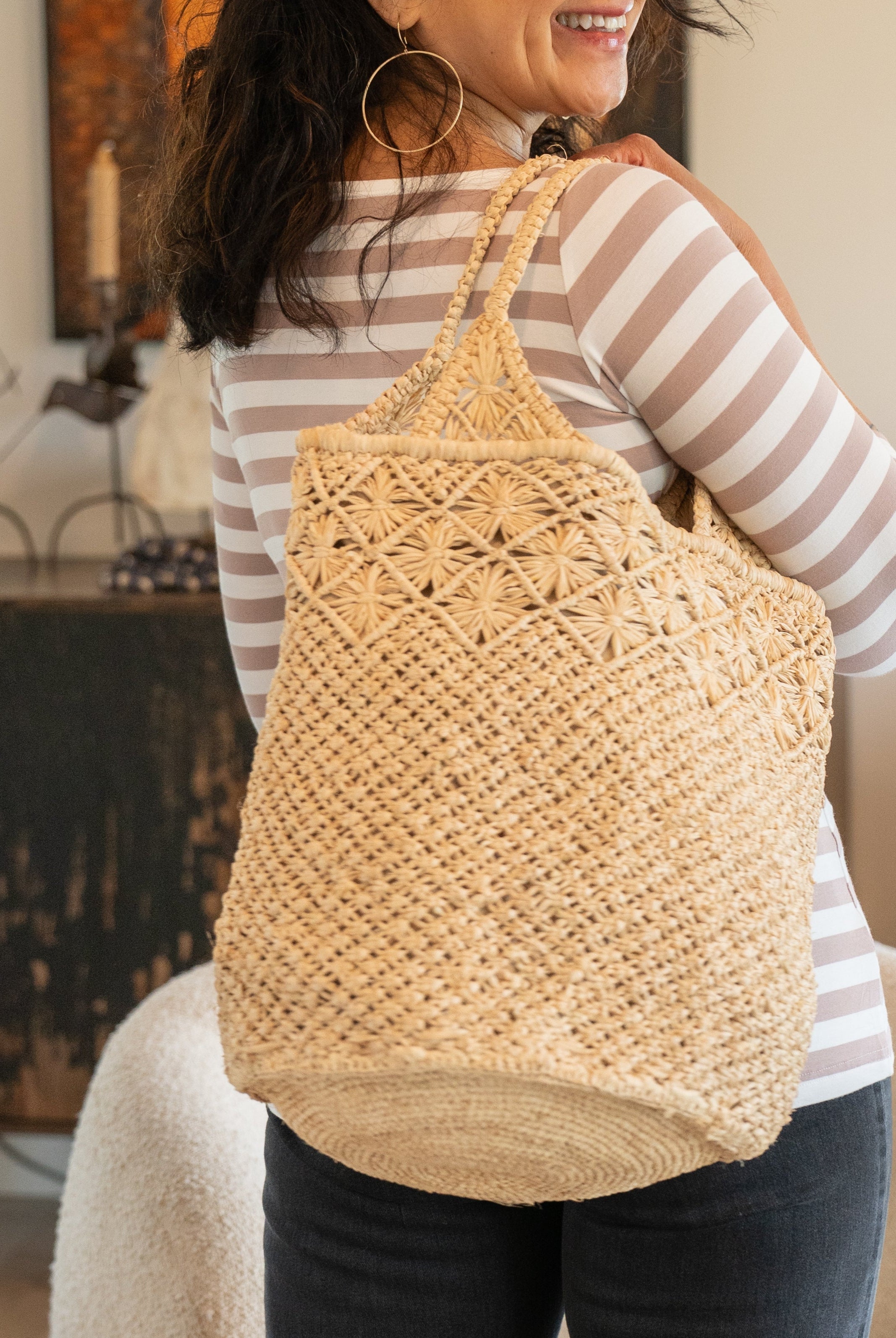 Model wearing Luca Macrame Diamonds Crochet Straw Handbag handmade knotted natural raffia palm fiber in a solid hue of Natural straw color in a multi-texture circular pattern of concentric spiral links on the base, cross-hatch x pattern up 2/3rds of the bag, and geometric diamond flower pattern around the top third, with diamond pattern on the base of the shoulder strap handles with tubular loop handle tops - Shebobo