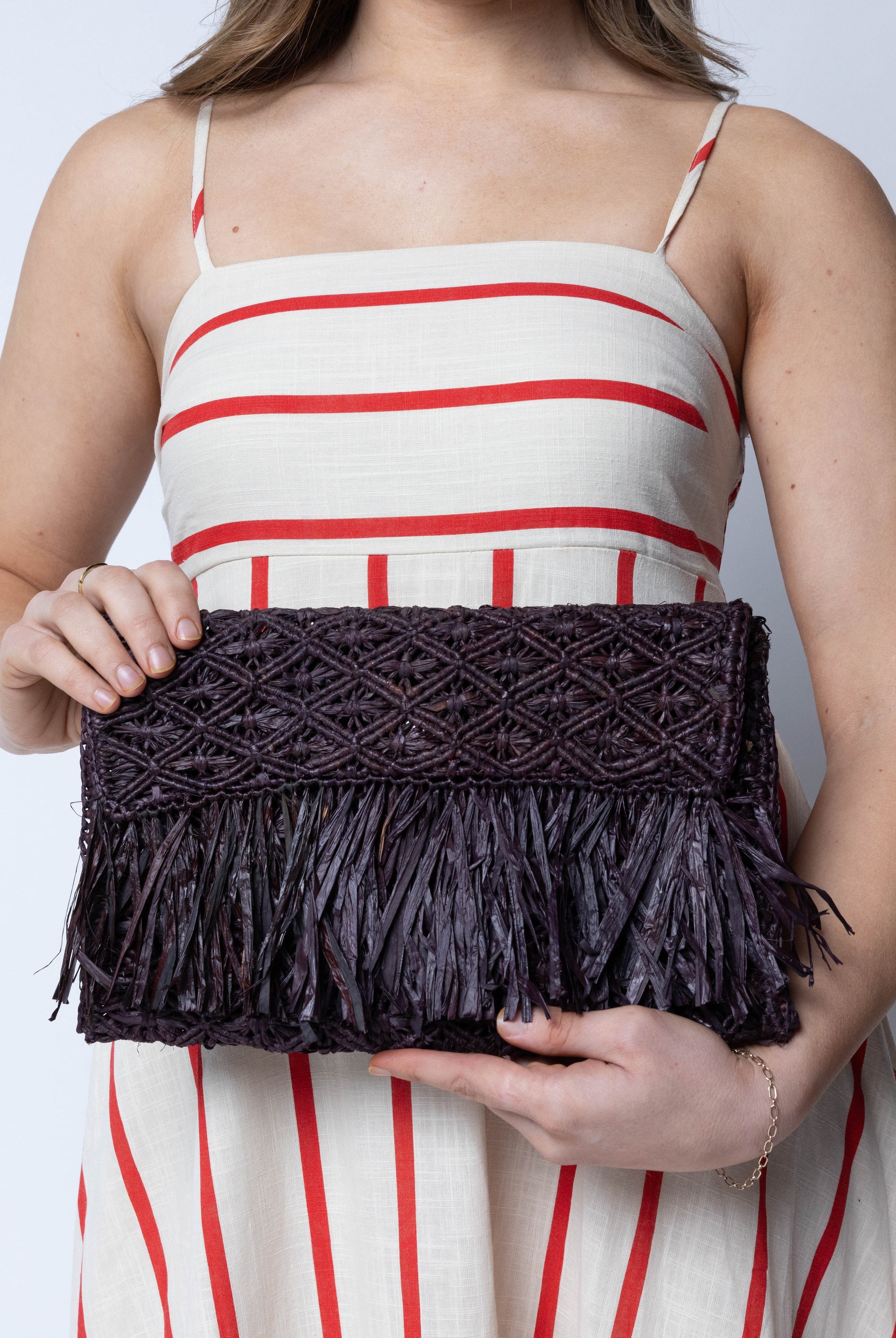 Model wearing Luli Macrame Diamond and Crochet Straw Envelope Clutch Purse with Raw Fringe Trim Edge handmade macrame and crochet natural raffia palm fiber in a solid hue of Mocha dark/chocolate/brown in a diagonal geometric pattern of starburst or flower inside diamonds with hand brushed raw fringe trim edge along the top flap of the envelope design handbag - Shebobo