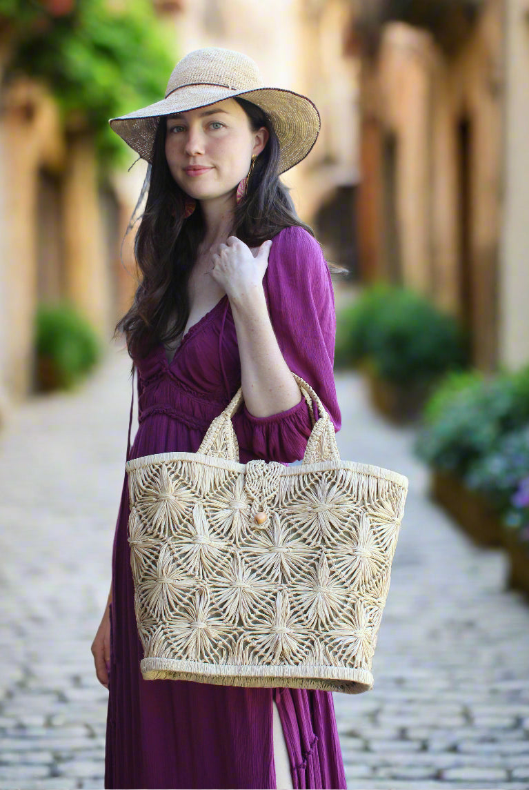 Model wearing Lusha Macrame Diamond and Crochet Straw Basket Bag handmade natural raffia palm fiber in a solid hue of natural straw color macrame into a large geometric diagonal diamond pattern with loop banding on the top and bottom edges, macrame diamond and loop handles, with knotted matching flap closure beach bag shoulder bag purse - Shebobo (with Rachel 4" Brim Crochet Straw Sun Hats with Colored Edge)