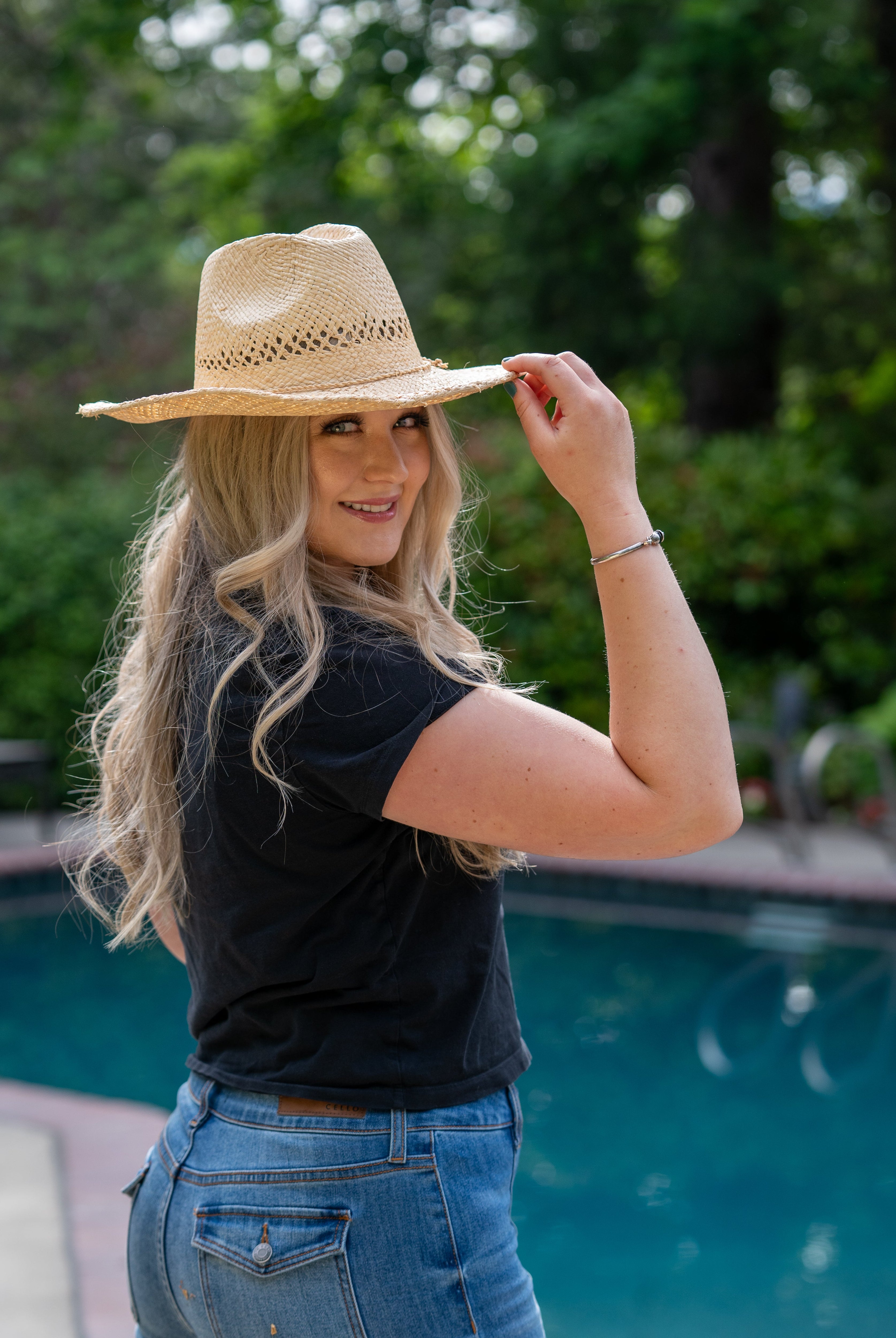 Model wearing Macho Natural Unisex Straw Cowboy Hat with Adjustable Wire Rim handmade woven raffia in a solid hue of natural straw color in a structured crown style with open weave pattern for breathability and pliable wire rim with matching twisted cord hat band - Shebobo