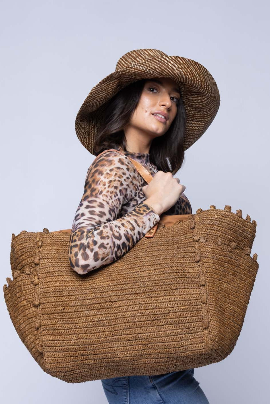 Model wearing Side view Madeline Tobacco XL Crochet Raffia Straw Basket Shoulder Bag with Pockets handmade raffia palm fiber in a solid hue of tobacco dark/cinnamon/brown with crochet horizontal subtle band texture, round boucle nub edges, oversized external pockets, and leather handles - Shebobo