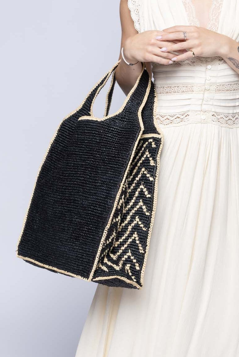 Model wearing Side view Mamie Zigzag Pinstripe XL Crochet Straw Basket Handbag handmade crochet natural raffia palm fiber in a solid hue of black purse beach bag with contrasting natural straw color zigzag pinstripe pattern on the sides of the bag and matching outer edge - Shebobo