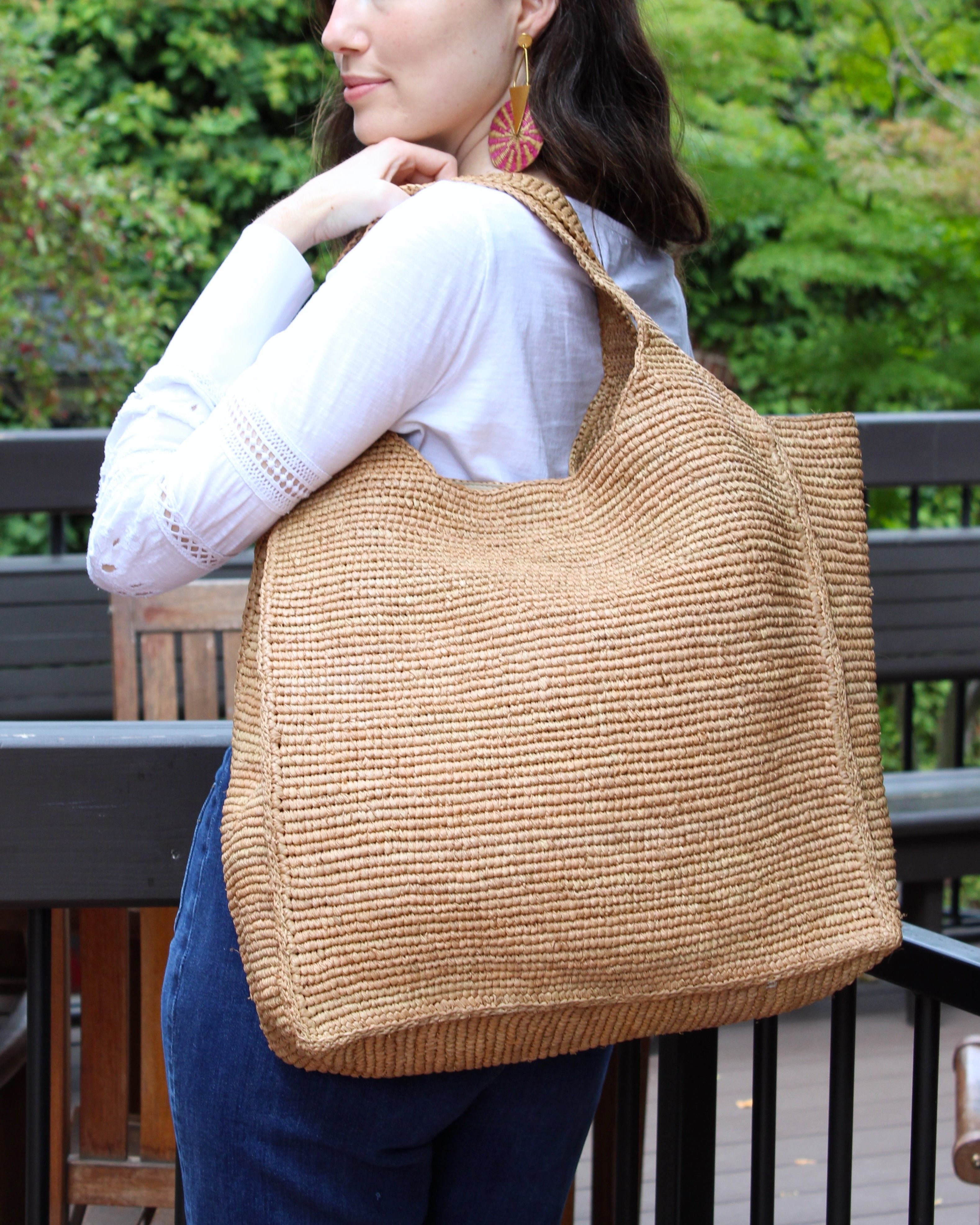 Model wearing Mamie XL Crochet Straw Basket Handbag handmade crochet natural raffia palm fiber in a solid hue of cappuccino tea/light/brown purse beach bag - Shebobo