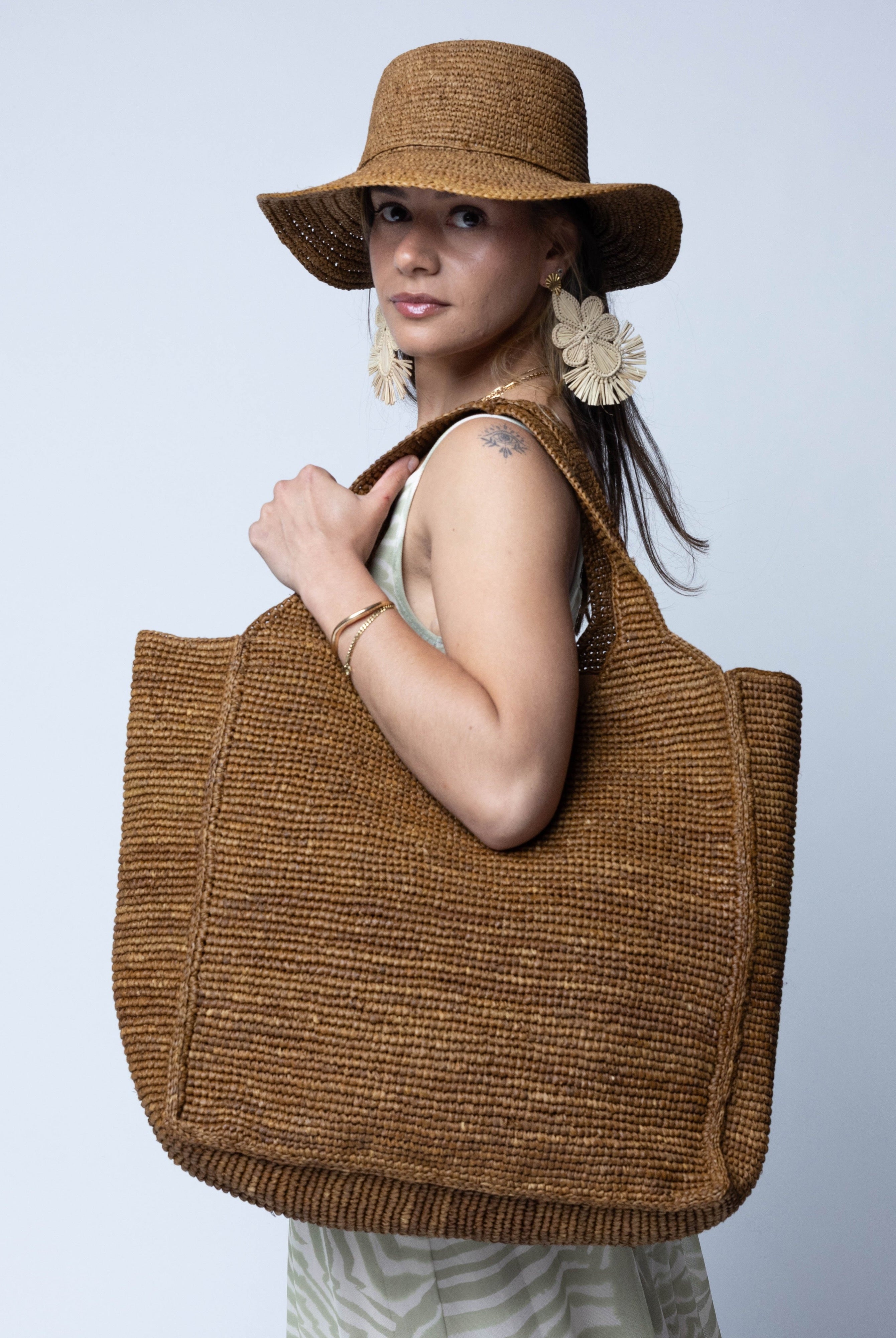 Model wearing Mamie XL Crochet Straw Basket Handbag handmade crochet natural raffia palm fiber in a solid hue of Tobacco cinnamon/dark/brown purse beach bag - Shebobo (with Bolero 3" Brim Crochet Straw Sun Hats)