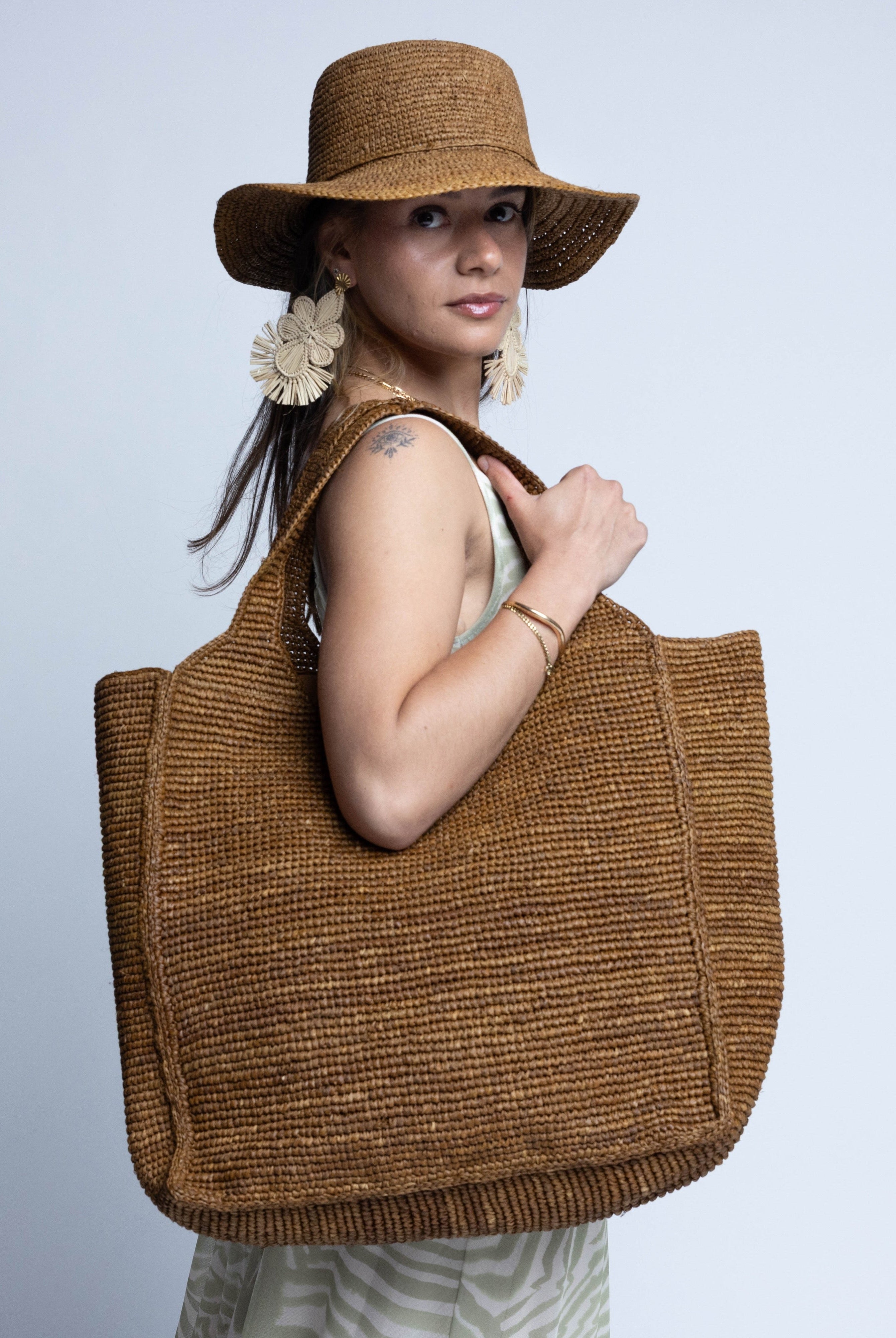 Model wearing Mamie XL Crochet Straw Basket Handbag handmade crochet natural raffia palm fiber in a solid hue of Tobacco cinnamon/dark/brown purse beach bag - Shebobo (with Bolero 3" Brim Crochet Straw Sun Hats)