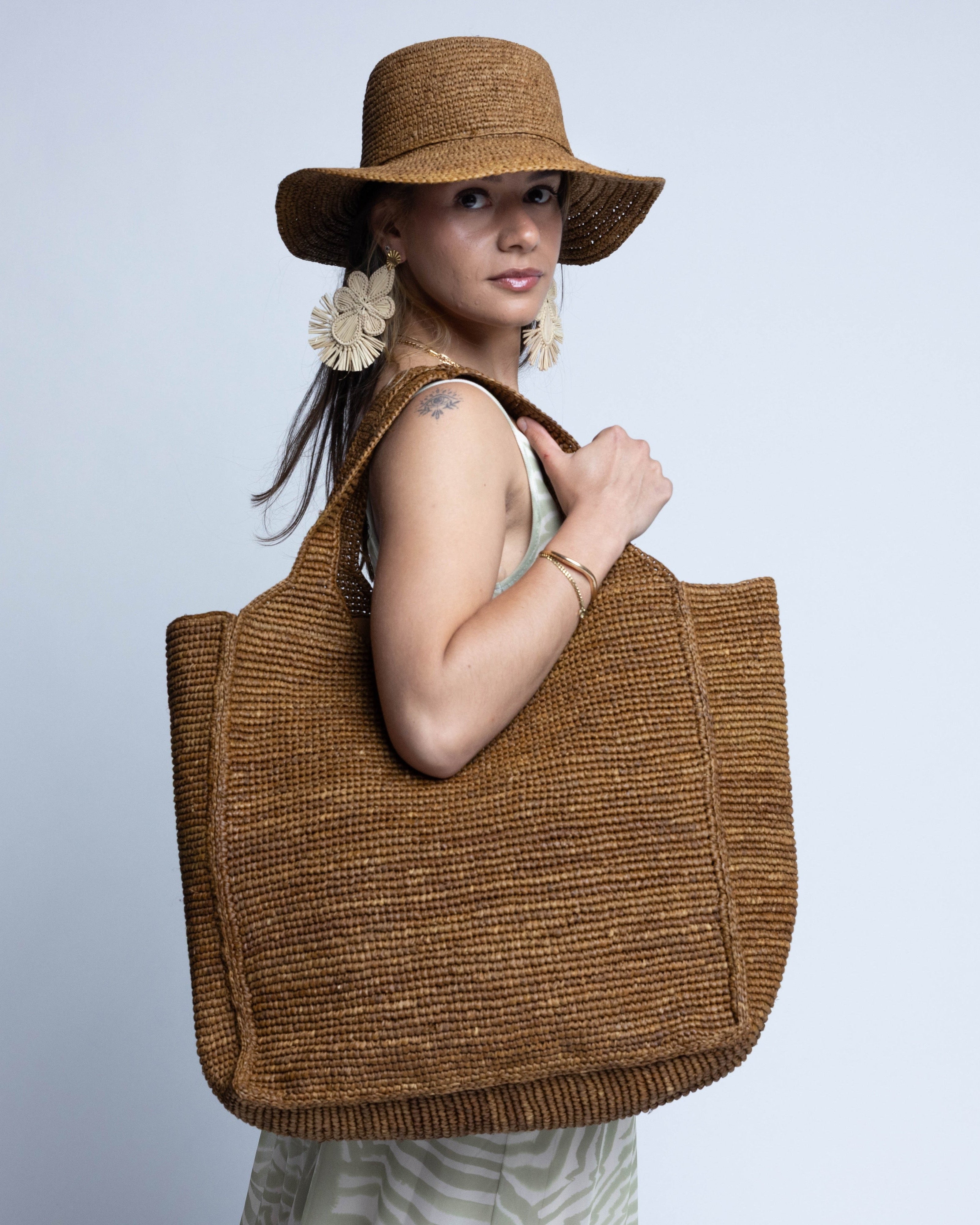 Model wearing Mamie XL Crochet Straw Basket Handbag handmade crochet natural raffia palm fiber in a solid hue of Tobacco cinnamon/dark/brown purse beach bag - Shebobo (with Bolero 3" Brim Crochet Straw Sun Hats)