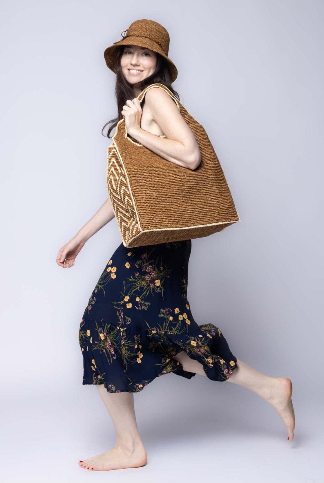Model wearing Side view Mamie Zigzag Pinstripe XL Crochet Straw Basket Handbag handmade crochet natural raffia palm fiber in a solid hue of tobacco dark/cinnamon/brown purse beach bag with contrasting natural straw color zigzag pinstripe pattern on the sides of the bag and matching outer edge - Shebobo