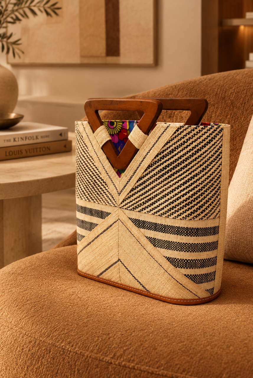 Lifestyle view Mariposa Zuki Raffia Straw Bucket Handbag with Wood Triangle Handles handmade loomed raffia palm fiber in a multi paneled pattern design of pinstripe, melange, and wide stripe combinations geometrically radiating from the center point of the bag outwards in a two tone color combination of Natural straw color and black with a solid hue of color on the back of the bag plus carved wooden handles purse - Shebobo
