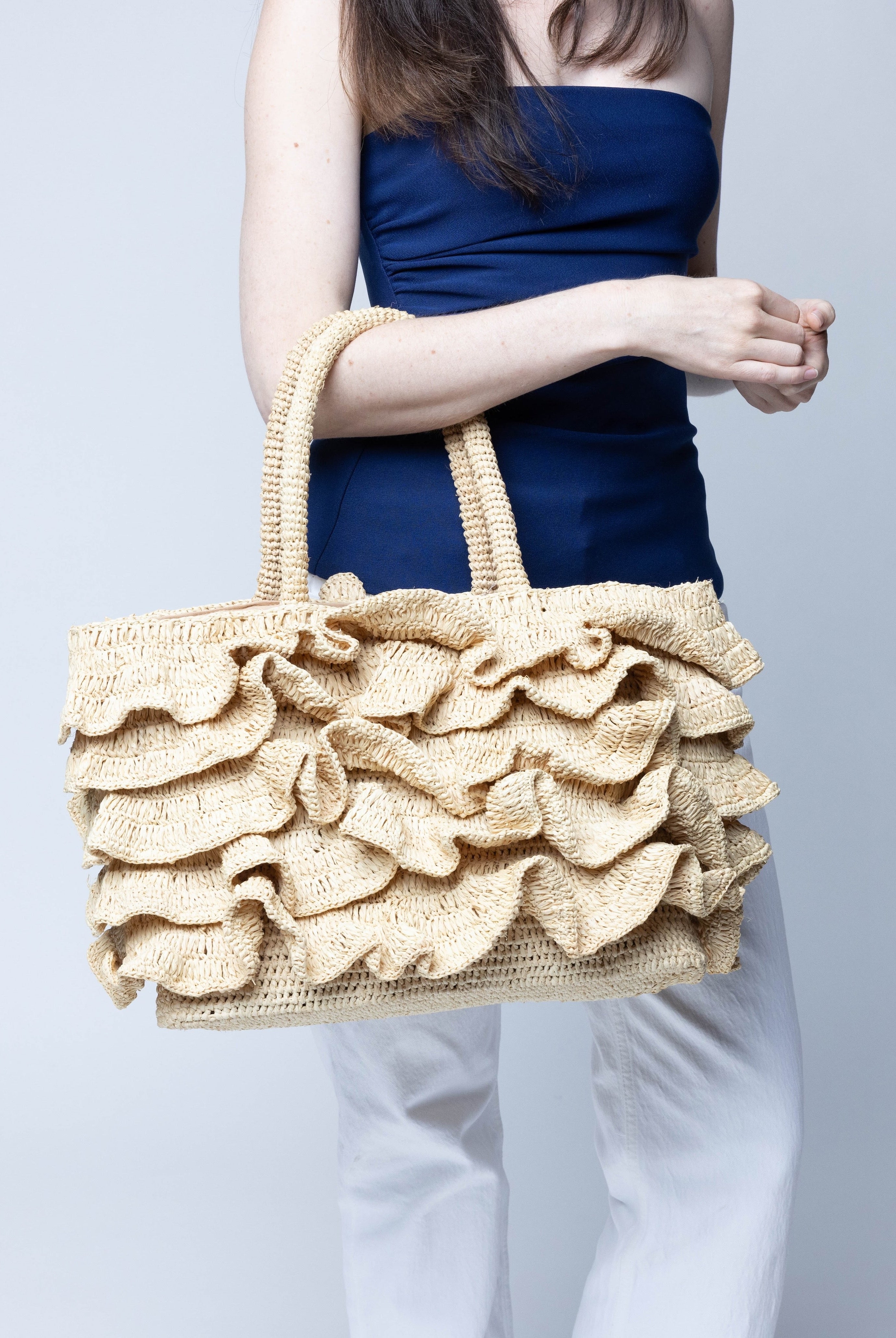Model wearing Maryann Ruffle Crochet Straw Basket Handbag handmade crochet natural raffia palm fiber in a solid hue of natural straw color with generous eight tier ruffle horizontally layered around the circumference of the bag and banded link textured handles purse bag - Shebobo
