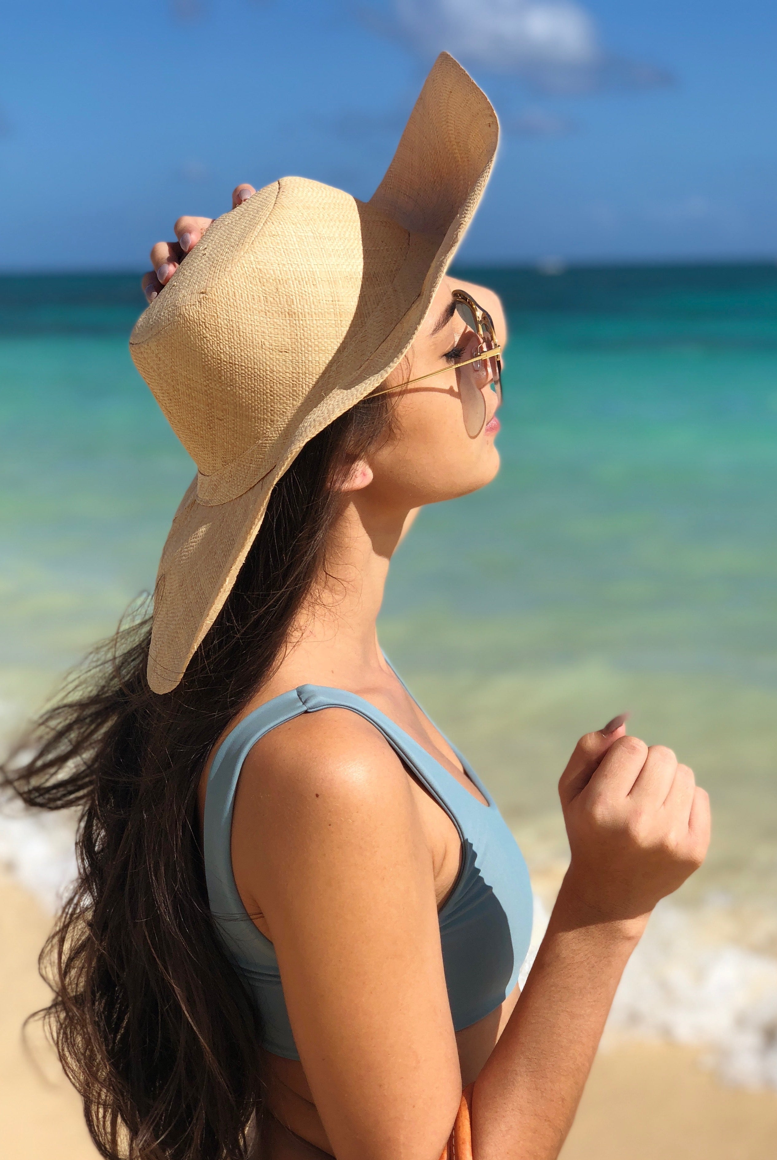 Model wearing Melanie 4.5" Wide Brim Raffia Straw Sun Hats handmade loomed natural raffia palm fiber in a solid hue of natural straw color round crown and flat brim with matching hatband and double bow detailing light weight breathable beach hat - Shebobo