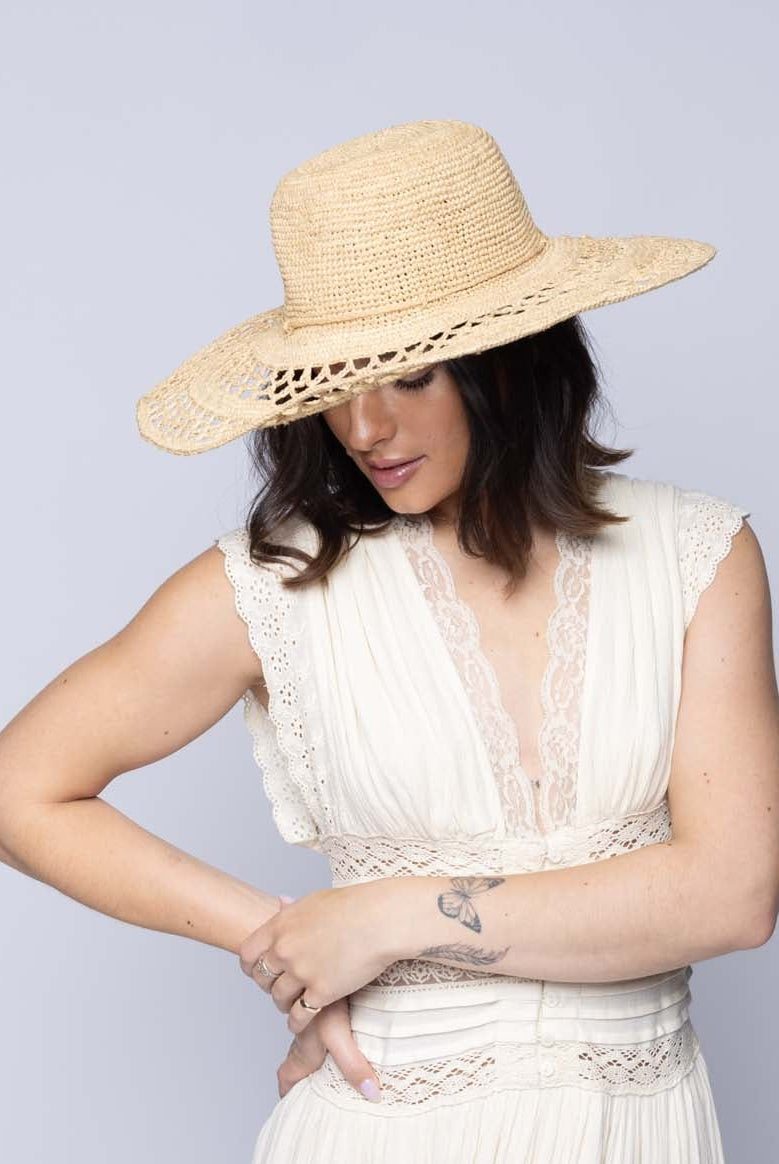 Model wearing Millie 4.5" Wide Brim Crochet Scallop Pattern Raffia Straw Sun Hat with Adjustable Wire Edge handmade woven natural raffia palm fiber in a solid hue of natural straw color with concentric spiral subtle link pattern starting on the top of the crown outwards with two circular bands of open scallop pattern weave on the brim separated by thicker bands of link texture with matching raffia braid hat band - Shebobo