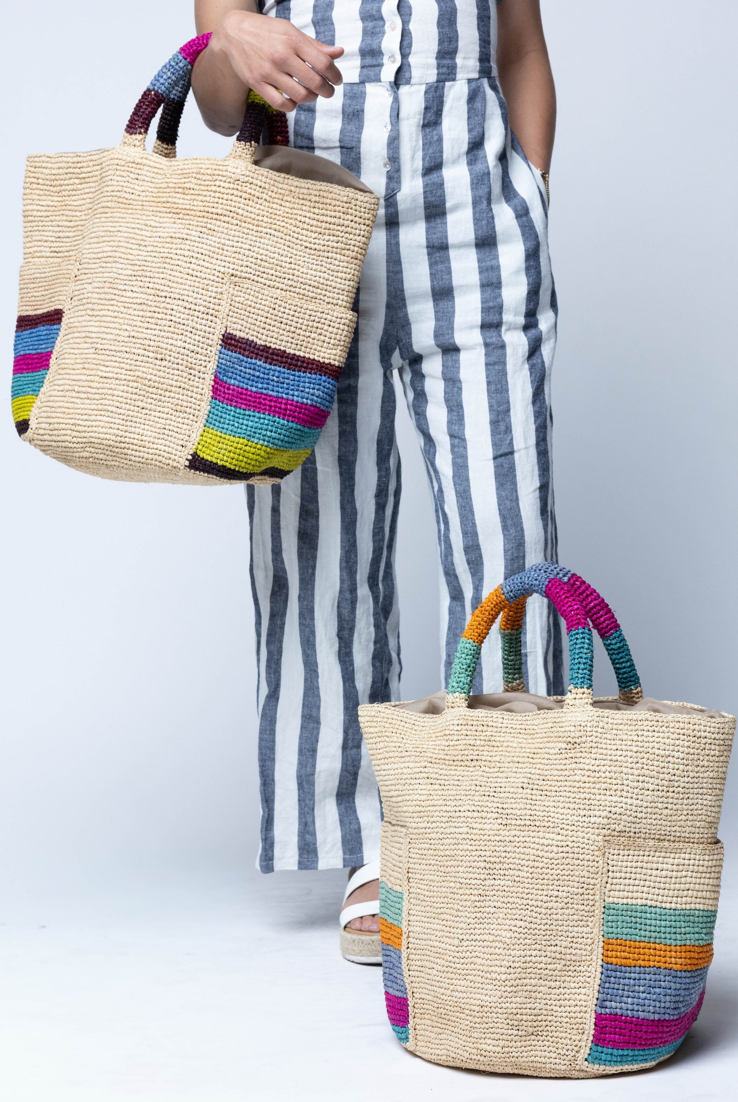 Model wearing Milos Caribbean and Riviera Stripes Crochet Straw Basket Handbag with Pockets handmade natural raffia palm fiber in a solid hue of natural straw color on the body of the bag with multicolor wide stripe pattern on both handles as well as two large external pockets tote bag - Shebobo