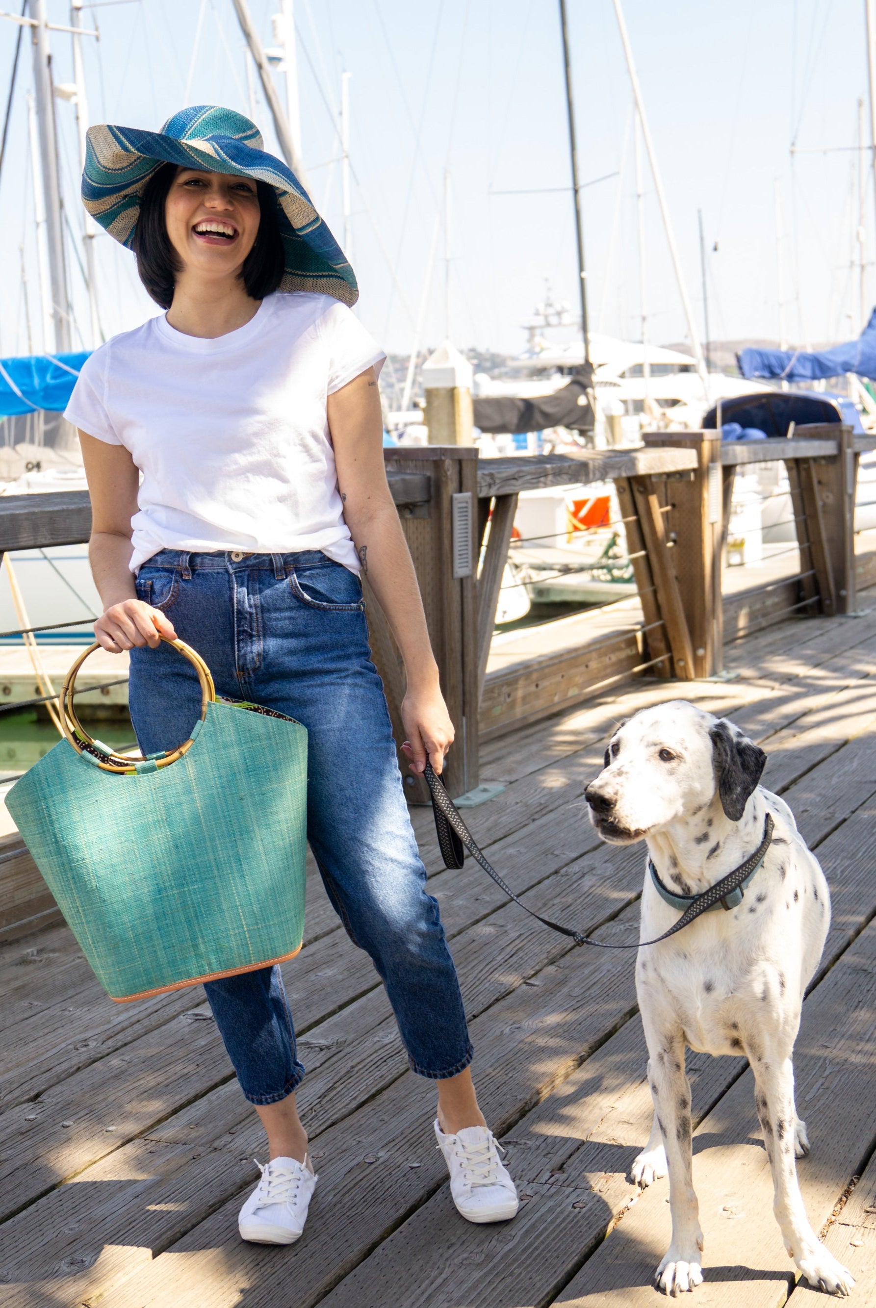 Model wearing Monica 7" Wide Brim Blue Swirl Multicolor Stripe Pattern Packable Straw Sun Hat handmade loomed raffia in multi width bands of navy blue, turquoise blue, and natural straw color create a striped swirl pattern - Shebobo (with Carmen Turquoise Straw Bucket Handbag with Bamboo Handles)