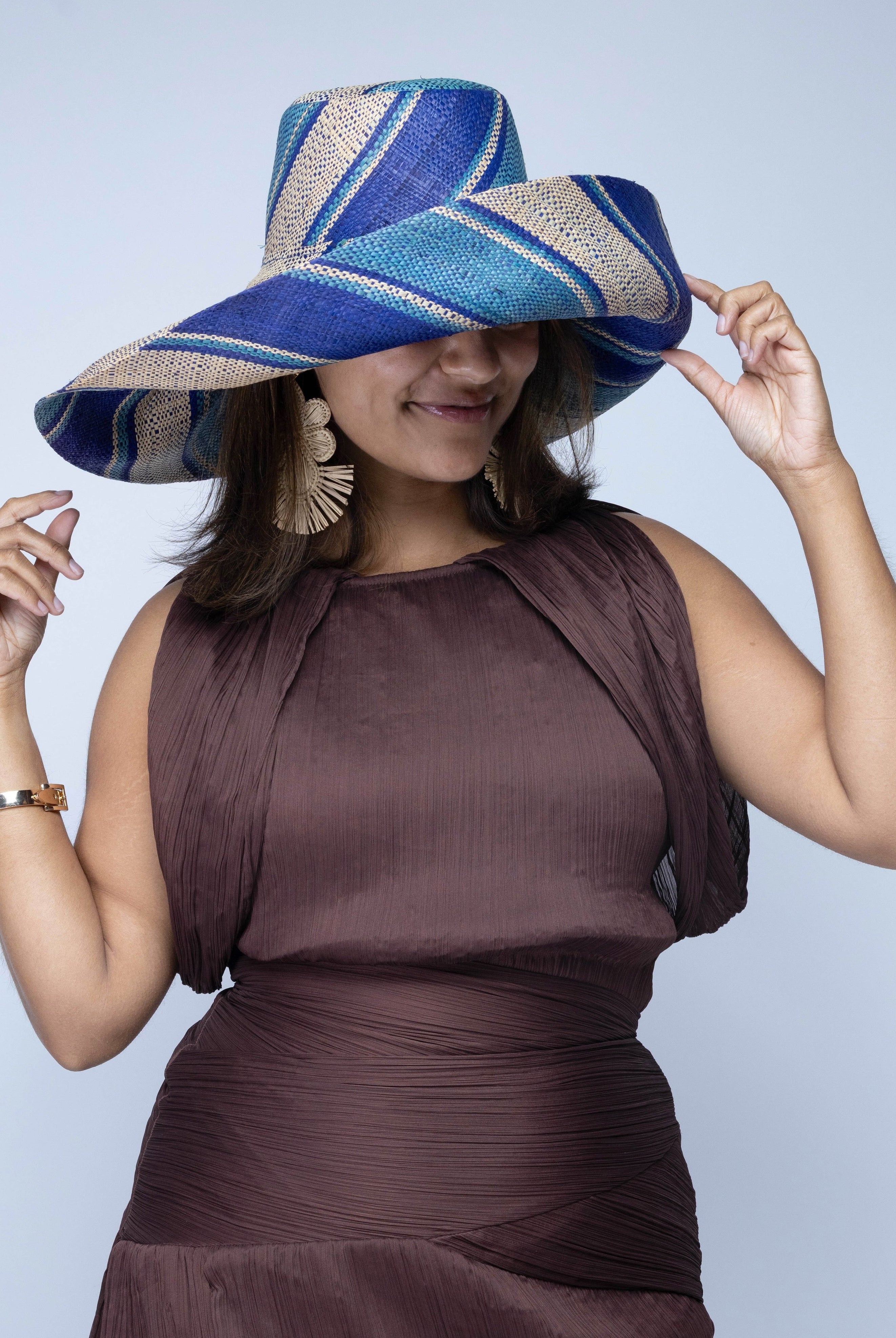 Model wearing Monica 7" Wide Brim Blue Swirl Multicolor Stripe Pattern Packable Straw Sun Hat handmade loomed raffia in multi width bands of navy blue, turquoise blue, and natural straw color create a striped swirl pattern - Shebobo