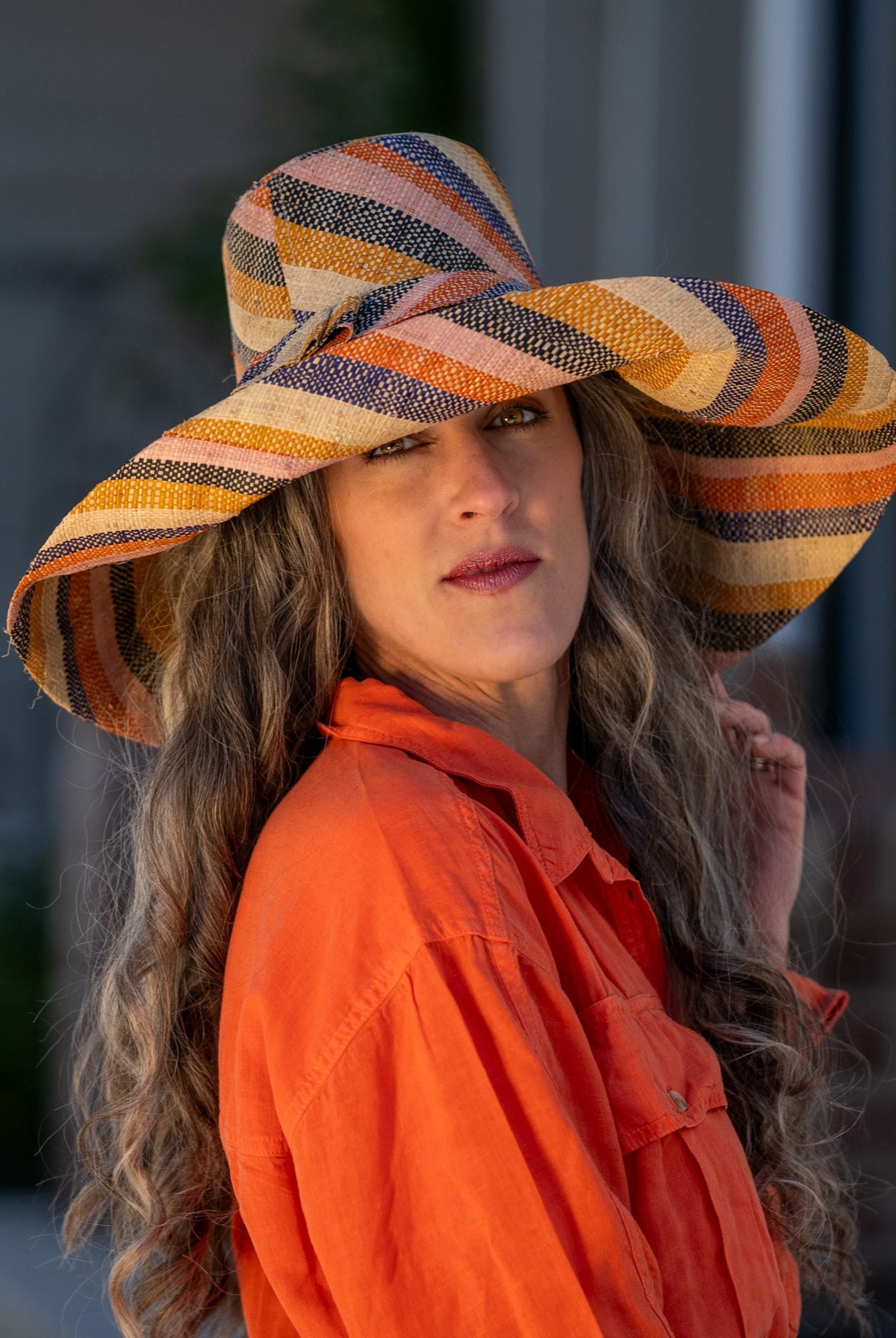 Model wearing Monica 7" Wide Brim Candyland Multicolor Stripes Packable Straw Sun Hat handmade loomed raffia in bands of natural straw color, black, saffron yellow/orange, light pink, coral orange/red, and dusk navy/dark/blue stripes create a swirl pattern - Shebobo
