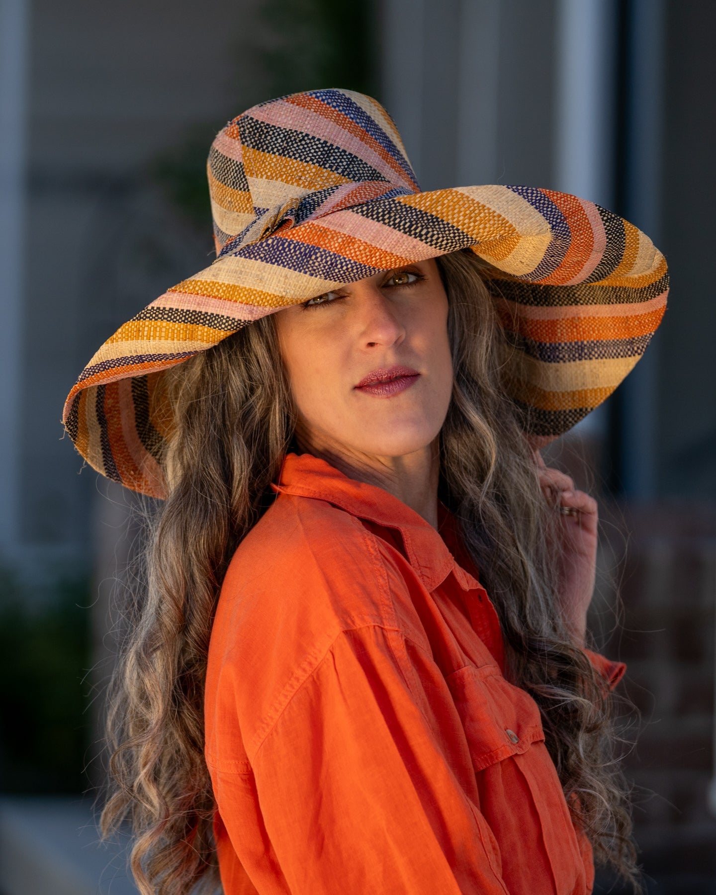 Model wearing Monica 7" Wide Brim Candyland Multicolor Stripes Packable Straw Sun Hat handmade loomed raffia in bands of natural straw color, black, saffron yellow/orange, light pink, coral orange/red, and dusk navy/dark/blue stripes create a swirl pattern - Shebobo