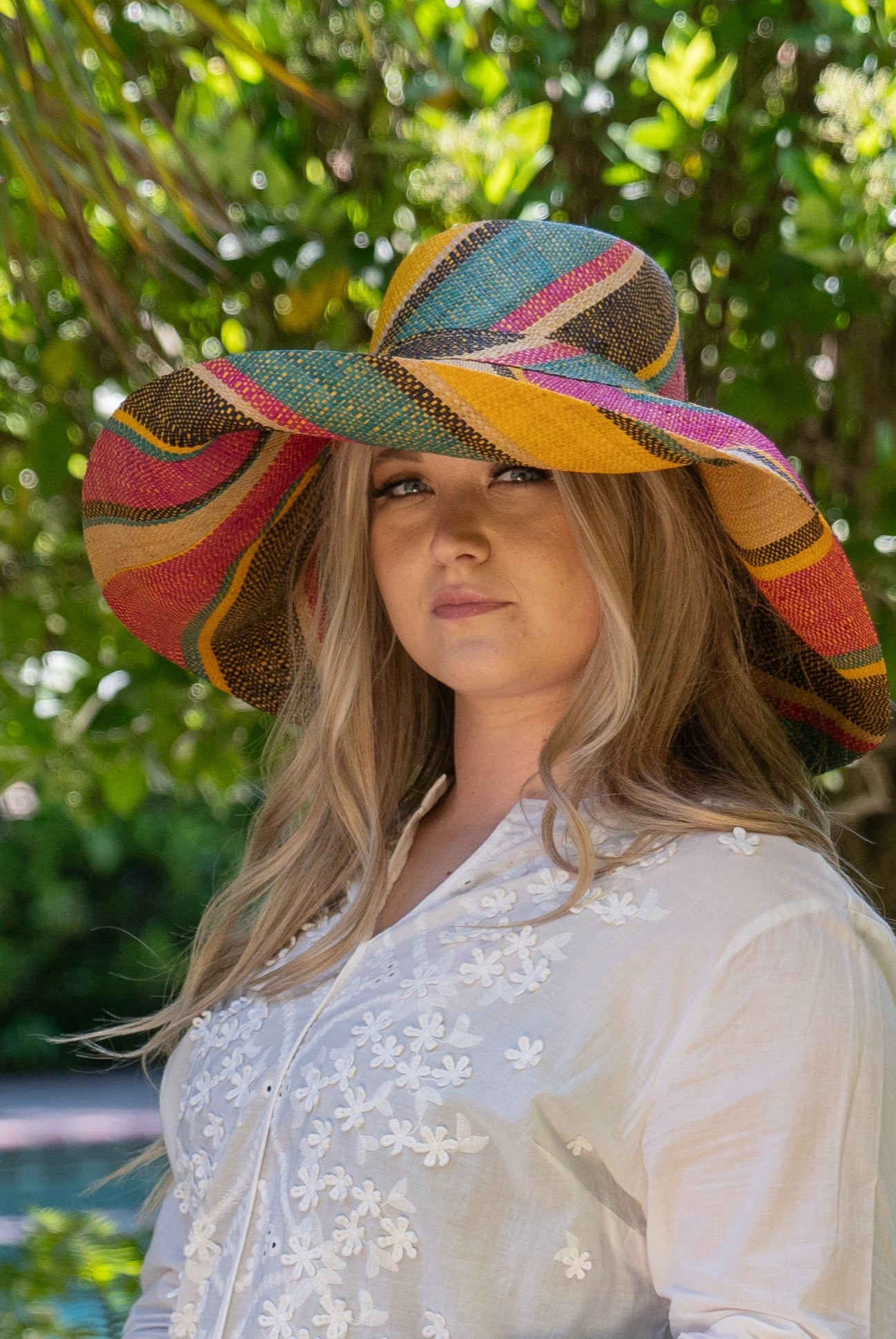 Model wearing Monica 7" Brim Carmalita Multicolor Stripes Packable Straw Sun Hat Handmade loomed raffia in multi width bands of saffron yellow, fuchsia pink, turquoise blue, black, and natural create a swirl pattern - Shebobo