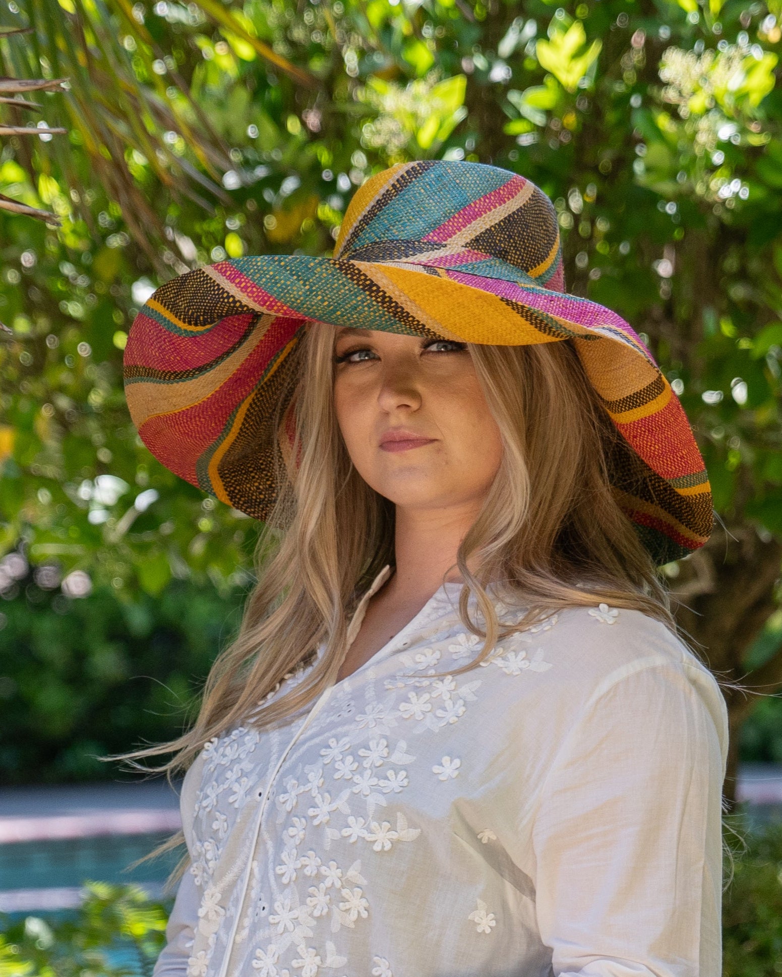 Model wearing Monica 7" Brim Carmalita Multicolor Stripes Packable Straw Sun Hat Handmade loomed raffia in multi width bands of saffron yellow, fuchsia pink, turquoise blue, black, and natural create a swirl pattern - Shebobo