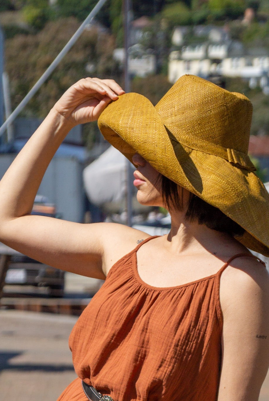 Model wearing Monica 7" Wide Brim Cinnamon Packable Straw Sun Hat handmade loomed natural raffia palm fiber in a solid hue of cinnamon/tobacco/brown - Shebobo