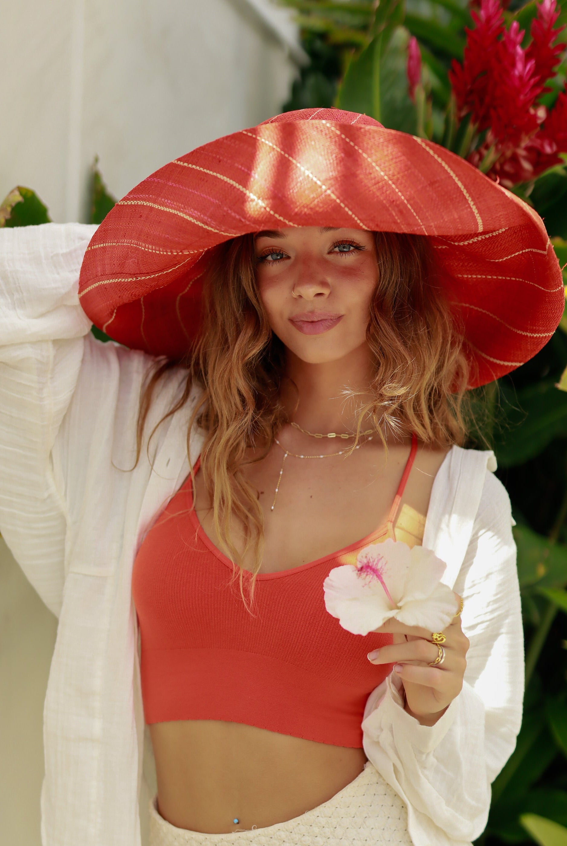 Model wearing Monica 7" Wide Brim Coral Pinstripes Packable Straw Sun Hat handmade loomed raffia in wide stripes of coral red/orange with narrow stripes of natural creating a swirl pattern - Shebobo
