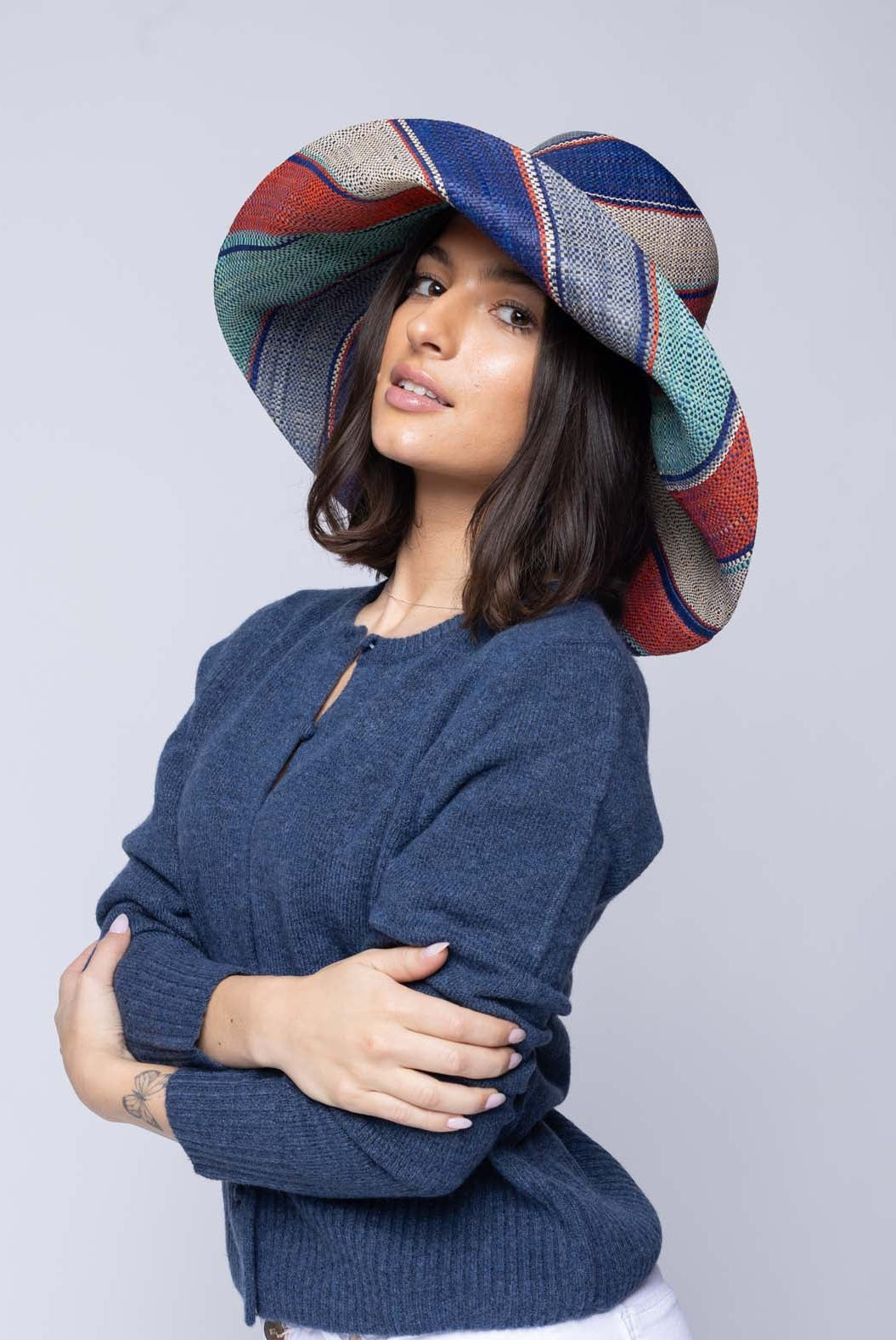 Model wearing Monica 5" & 7" Wide Brim Coral & Blue Swirl Multicolor Stripes Packable Straw Sun Hat Handmade loomed raffia in multi width bands of denim light/blue, navy dark/blue, coral orange/red, seafoam light/blue/green, and natural straw color create a swirl pattern - Shebobo