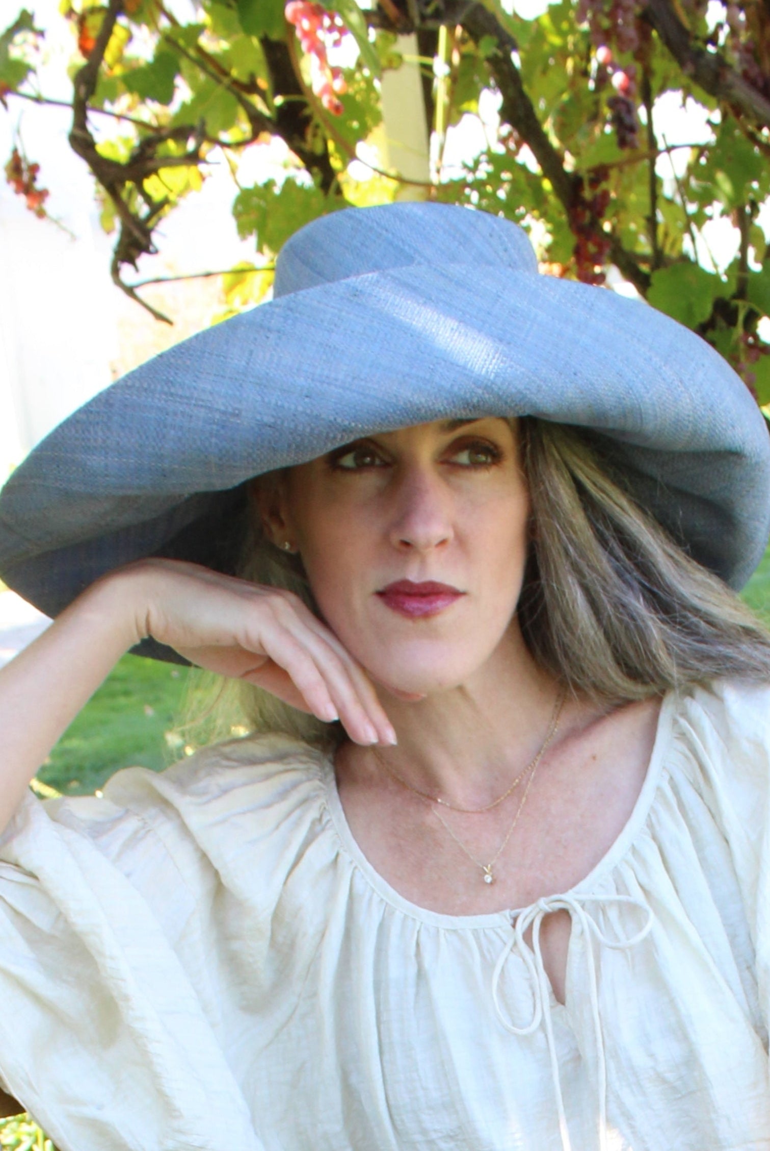 Model wearing Monica 7" Wide Brim Denim Packable Straw Sun Hat handmade loomed raffia in a solid hue of denim retro/light/blue lightweight malleable flexible sun protection hat - Shebobo