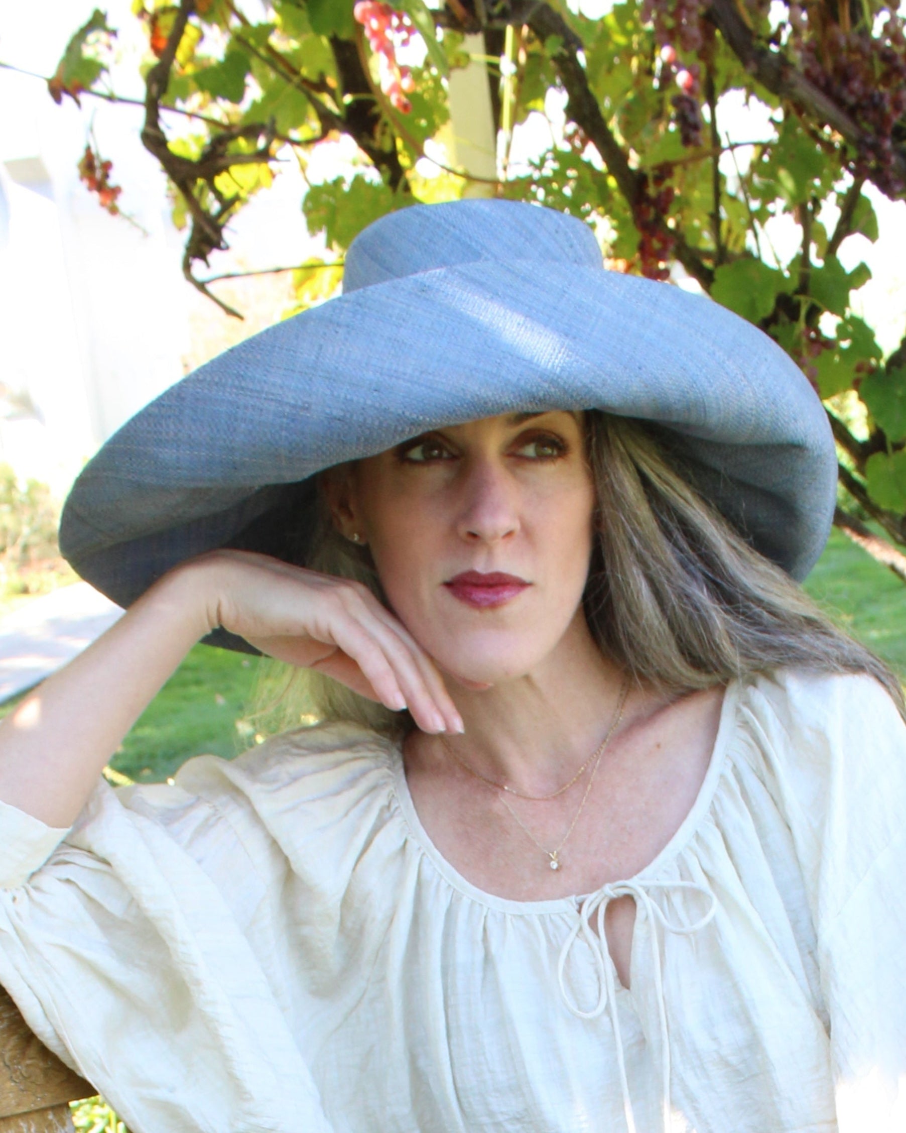 Model wearing Monica 7" Wide Brim Denim Packable Straw Sun Hat handmade loomed raffia in a solid hue of denim retro/light/blue lightweight malleable flexible sun protection hat - Shebobo