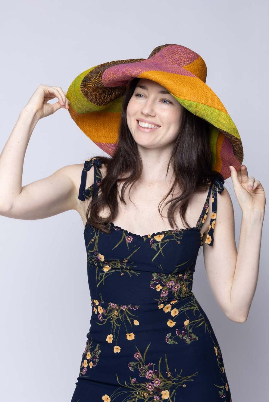 Model wearing Monica 5" & 7" Wide Brim Ipanema Swirl Multicolor Stripes Packable Straw Sun Hat Handmade loomed raffia in multi width bands of saffron yellow/orange, wisteria lilac/light/purple, midori lime/green, black, create a swirl pattern - Shebobo