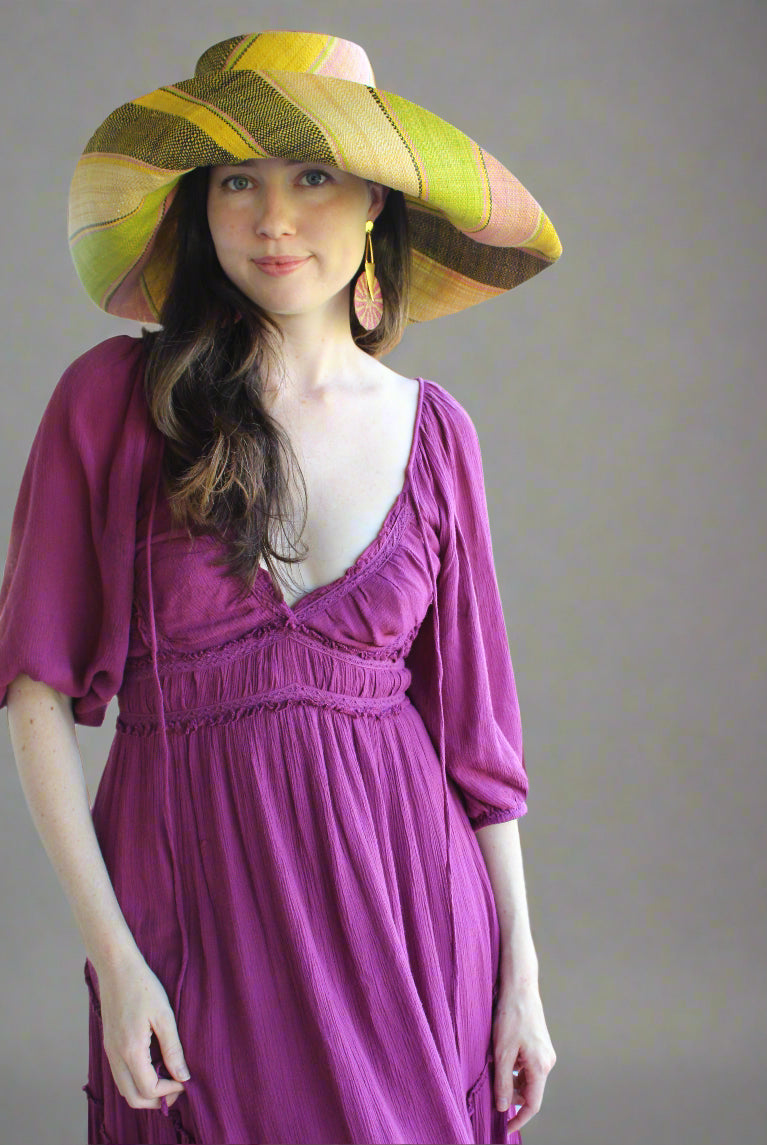 Model wearing Monica 7" Wide Brim Lemonade Swirl Multicolor Stripes Packable Straw Sun Hat Handmade loomed raffia in multi width bands of yellow, wisteria light/purple/pink, midori lime/green, black, natural straw color etc. create a swirl pattern - Shebobo