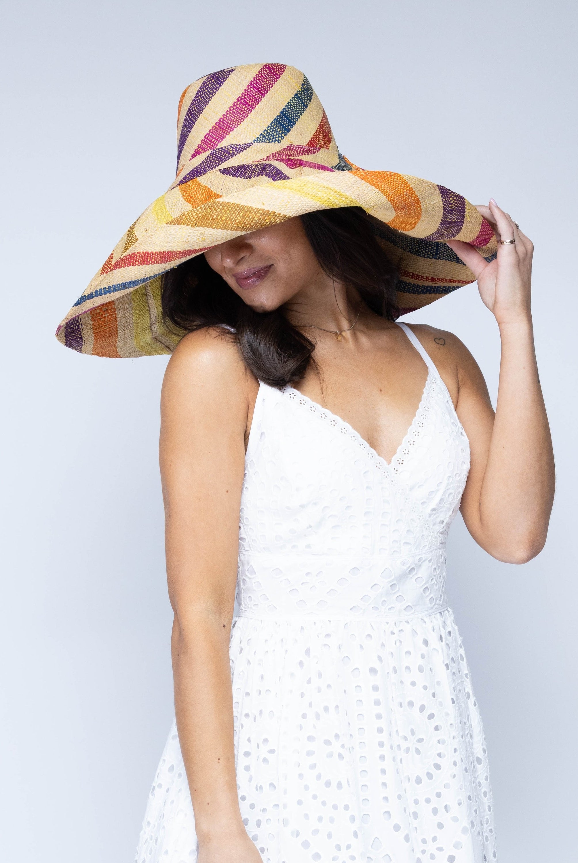 Model wearing Monica 7" Wide Brim Lingonberry Swirl Multicolor Stripes Packable Straw Sun Hat handmade loomed raffia in bands of natural straw color, red, purple, yellow, orange, turquoise blue, etc. stripes create a swirl pattern - Shebobo