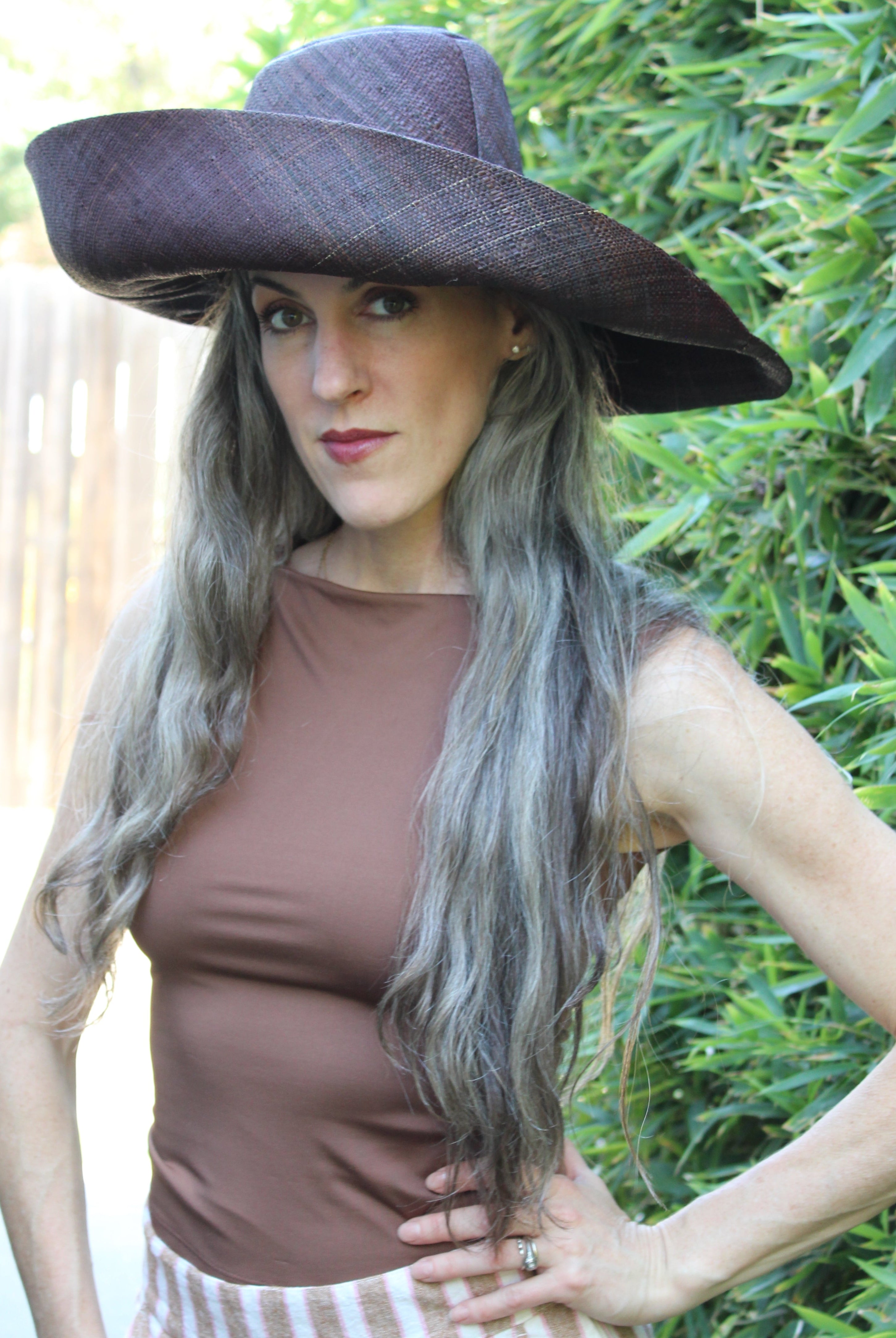 Model wearing Monica 7" Wide Brim Mocha Packable Straw Sun Hat handmade loomed raffia in a solid hue of mocha chocolate/dark/brown lightweight malleable flexible sun protection hat - Shebobo