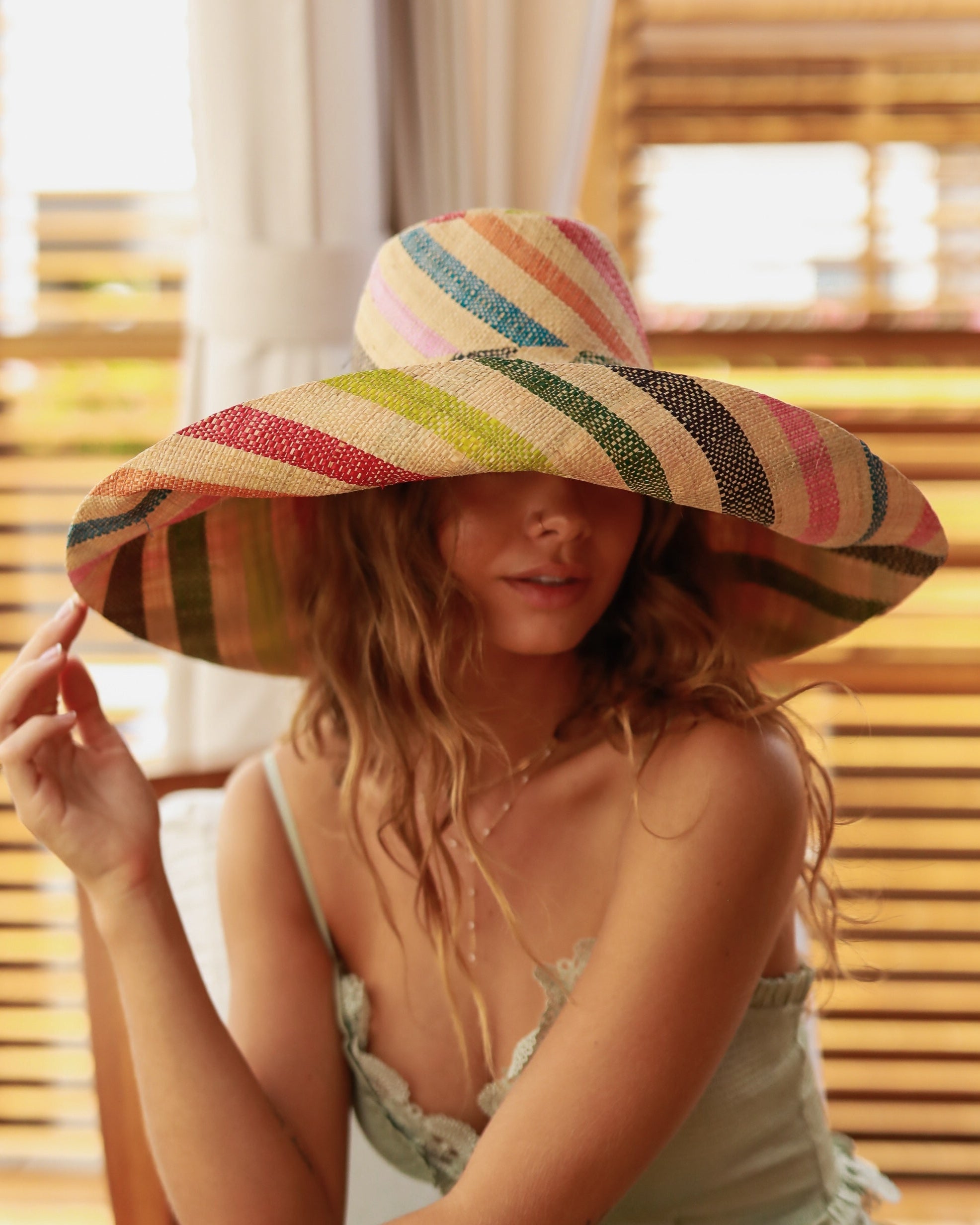 Model wearing Monica 7" Wide Brim Multi Stripe Multicolor Stripes Packable Straw Sun Hat handmade loomed raffia in bands of natural straw color, red, orange, lime green, turquoise blue, pink, olive green, and black stripes create a swirl pattern - Shebobo