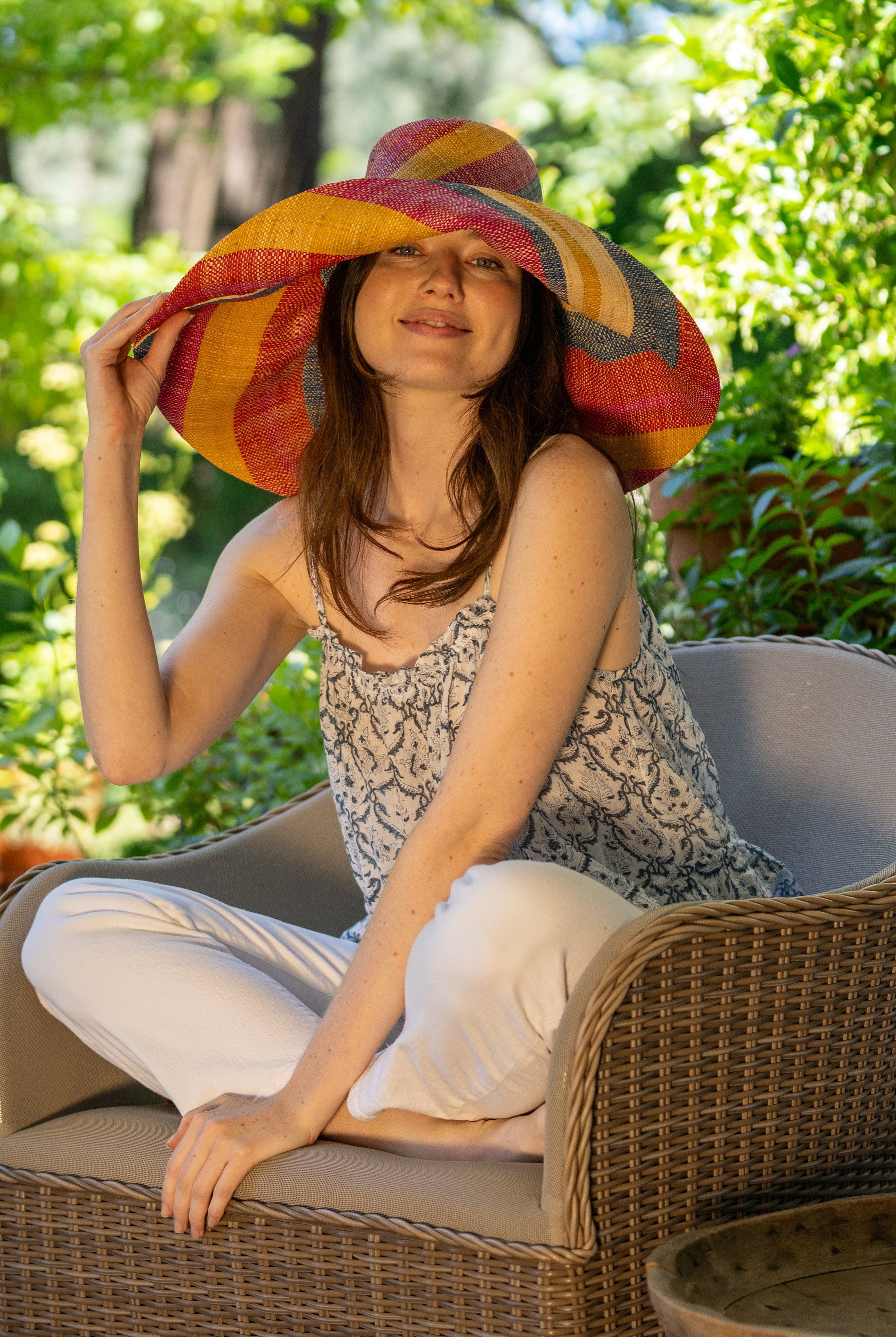 Model wearing Monica 7" Wide Brim Sassafras Swirl Multicolor Stripes Packable Straw Sun Hat Handmade loomed raffia in multi width bands of fuchsia pink, red, saffron yellow, navy blue, and natural straw color create a swirl pattern - Shebobo