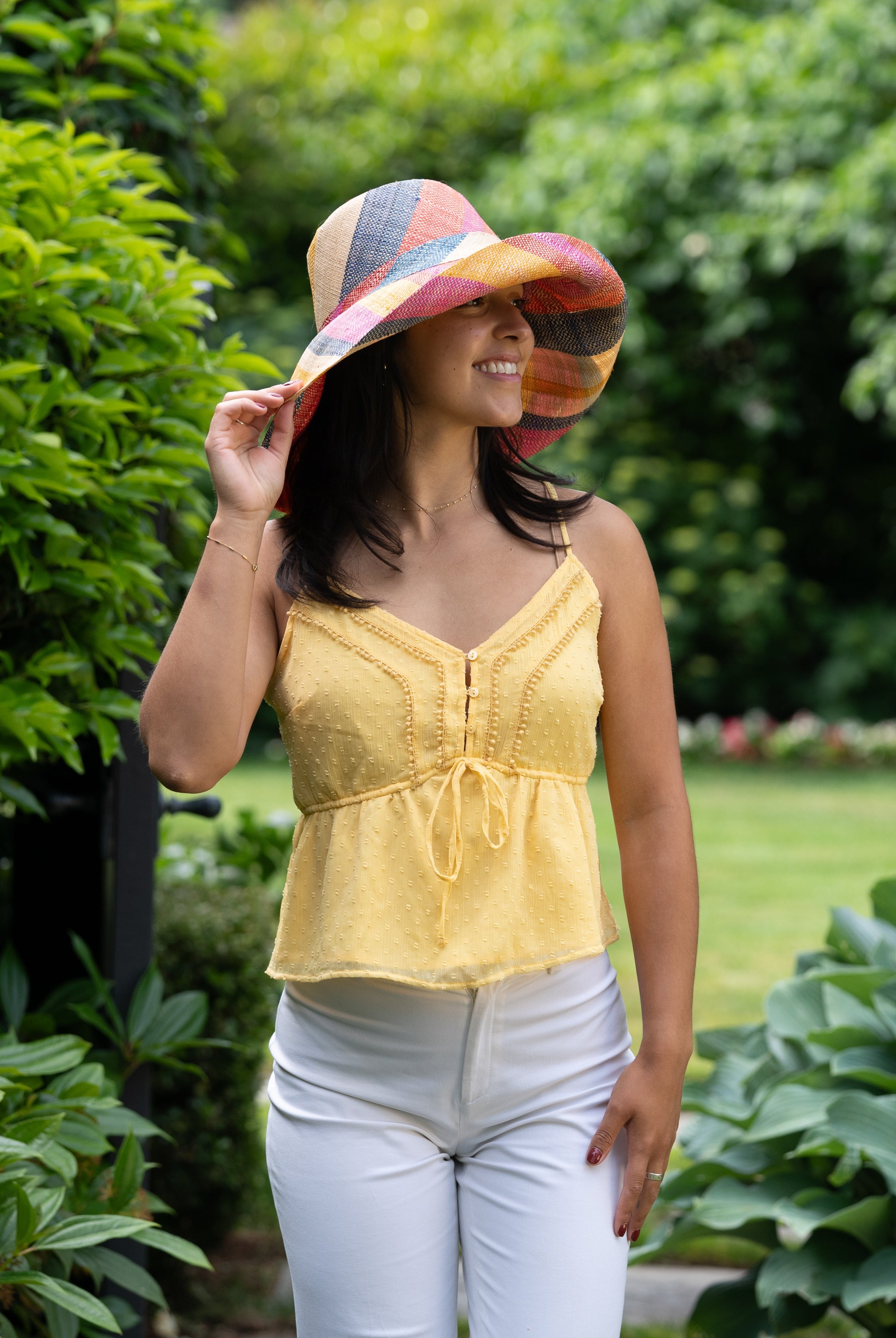 Model wearing Monica 5" Wide Brim Sassafras Swirl Multicolor Stripes Packable Straw Sun Hat Handmade loomed raffia in multi width bands of fuchsia pink, red, saffron yellow, navy blue, and natural straw color create a swirl pattern - Shebobo