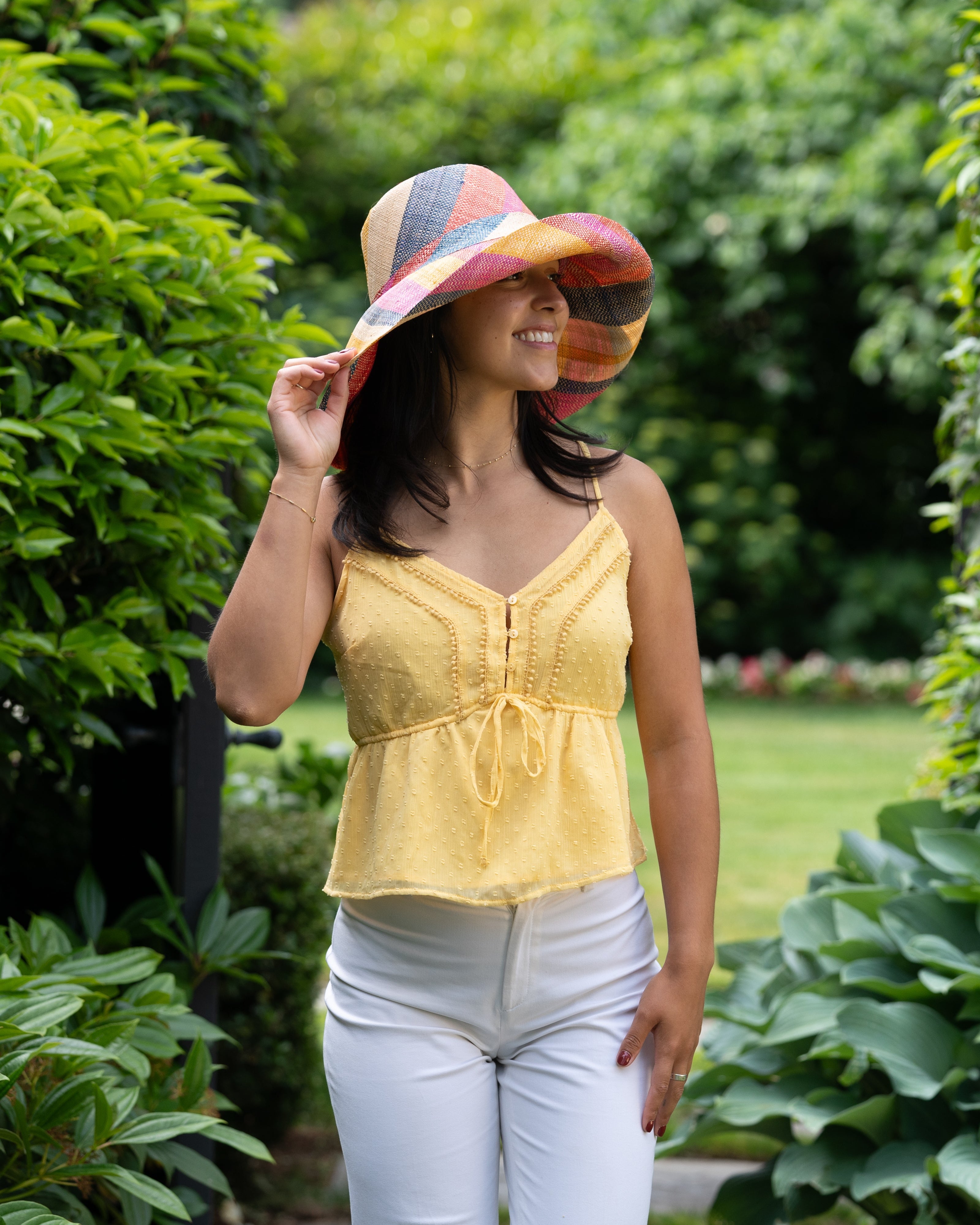 Model wearing Monica 5" Wide Brim Sassafras Swirl Multicolor Stripes Packable Straw Sun Hat Handmade loomed raffia in multi width bands of fuchsia pink, red, saffron yellow, navy blue, and natural straw color create a swirl pattern - Shebobo