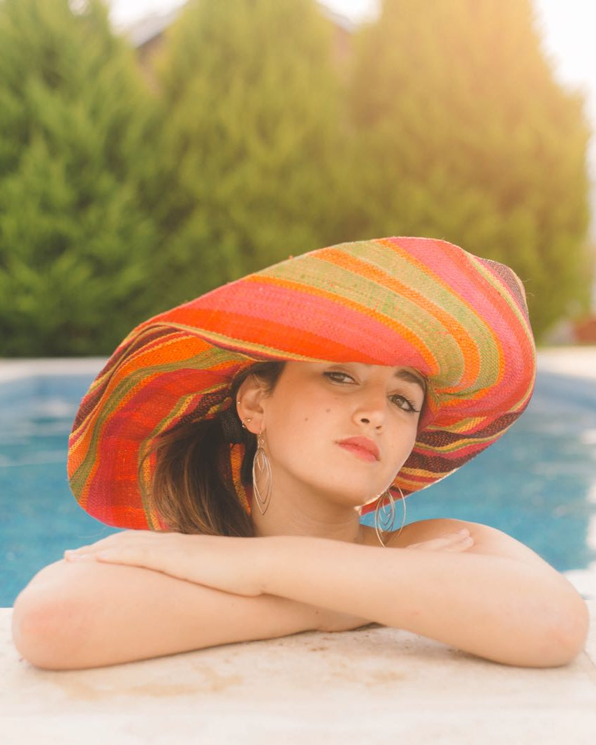 Model wearing Monica 7" Wide Brim Watermelon Swirl Multicolor Stripes Packable Straw Sun Hat Handmade loomed raffia in multi width bands of fuchsia pink, coral orange, red, yellow, black, lime green, etc. create a swirl pattern - Shebobo