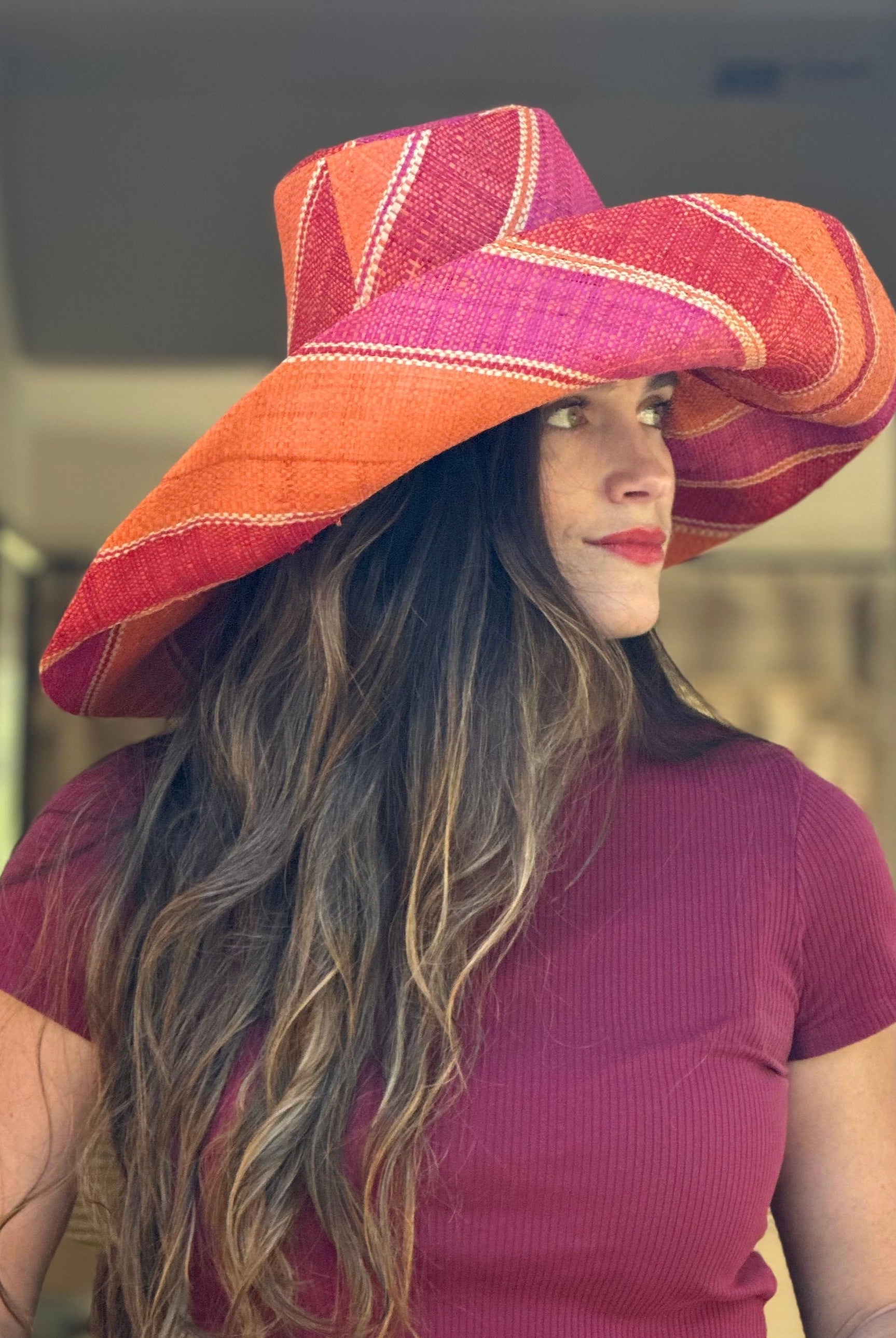 Model wearing Monica 7" Wide Brim Fuchsia & Coral Swirl Multicolor Stripes Packable Straw Sun Hat Handmade loomed raffia in multi width bands of fuchsia pink, coral orange, red, and natural straw color create a swirl pattern - Shebobo