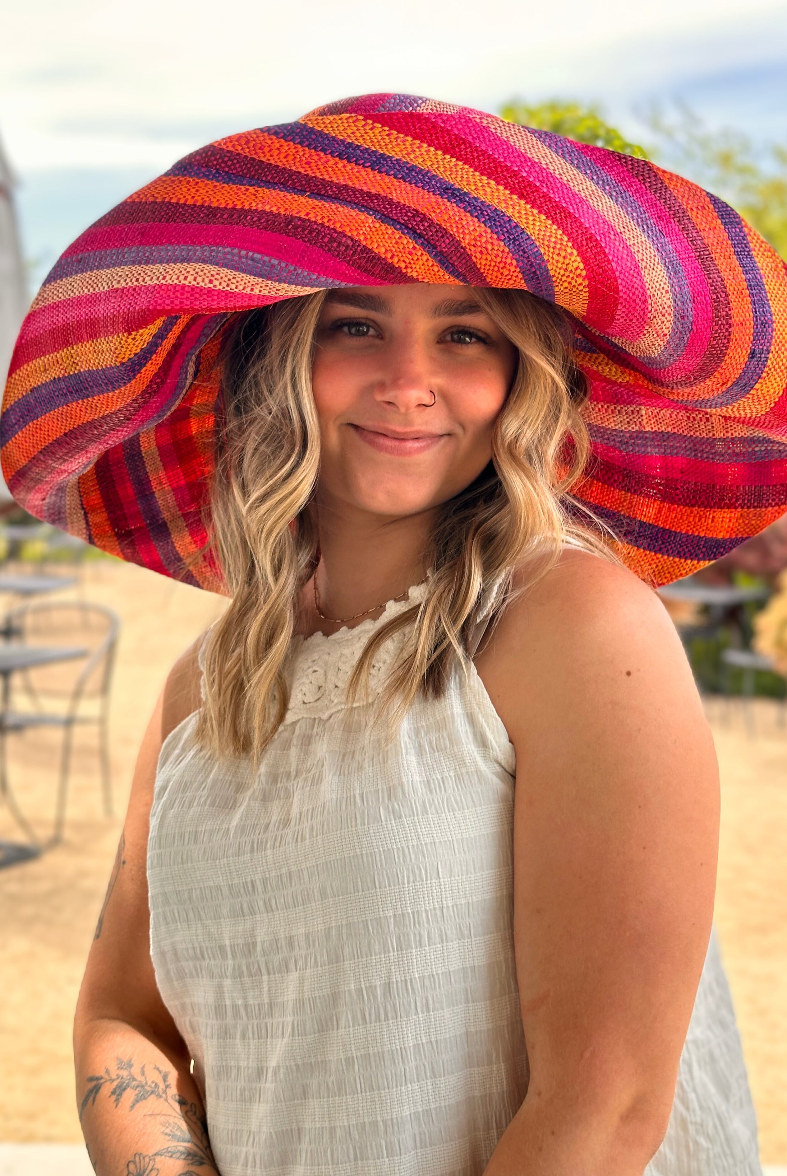 Model wearing Monica 7" Wide Fiesta Stripe Multicolor Stripes Packable Straw Sun Hat Handmade loomed raffia multi width bands of fuchsia pink, bordeaux red, saffron yellow, coral orange, natural straw color, purple, blue, etc. create a swirl pattern - Shebobo