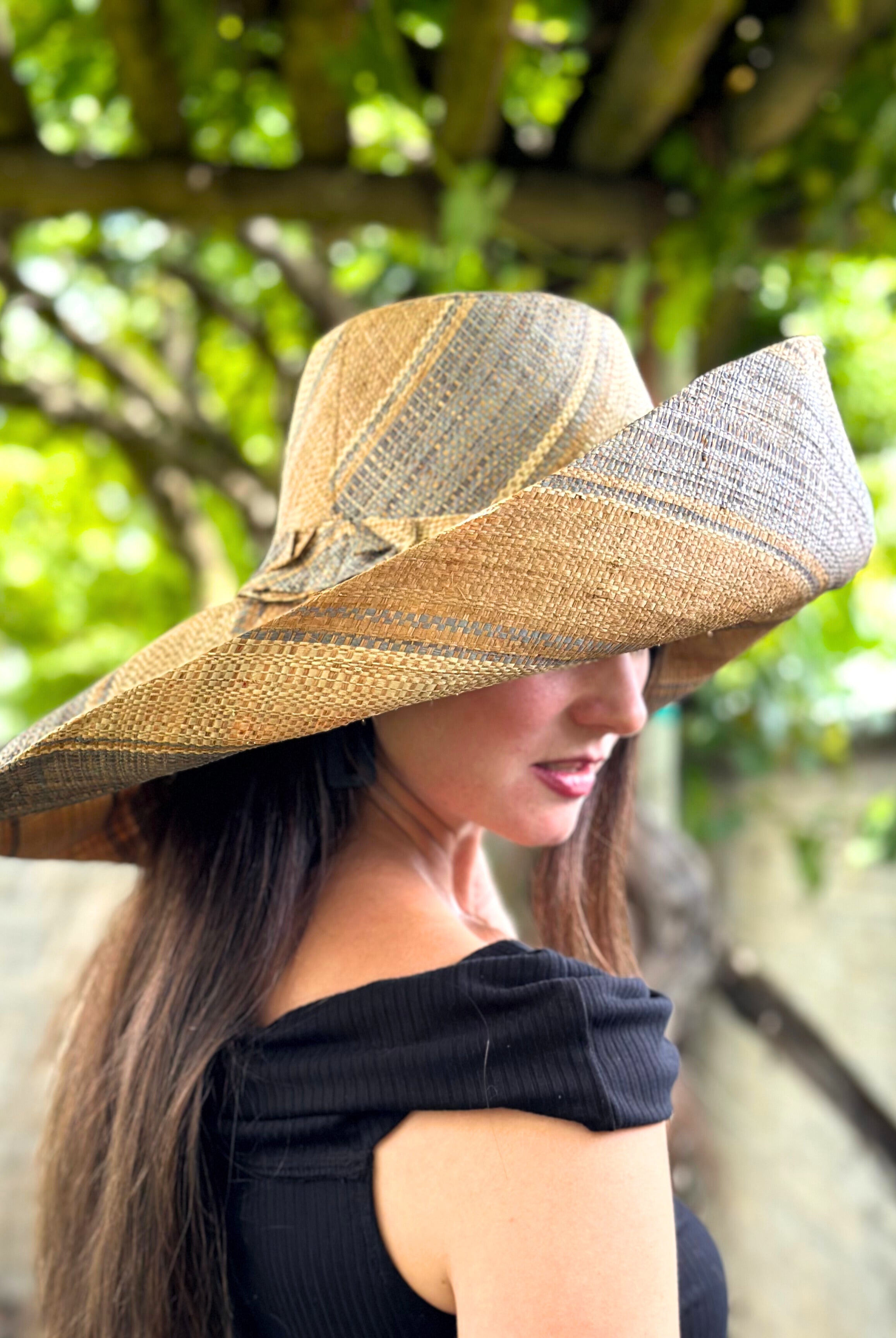 Model wearing Monica 7" Wide Brim Latte Swirl Multicolor Stripes Packable Straw Sun Hat Handmade loomed raffia in multi width bands of latte/light brown, grey, and natural create a swirl pattern - Shebobo