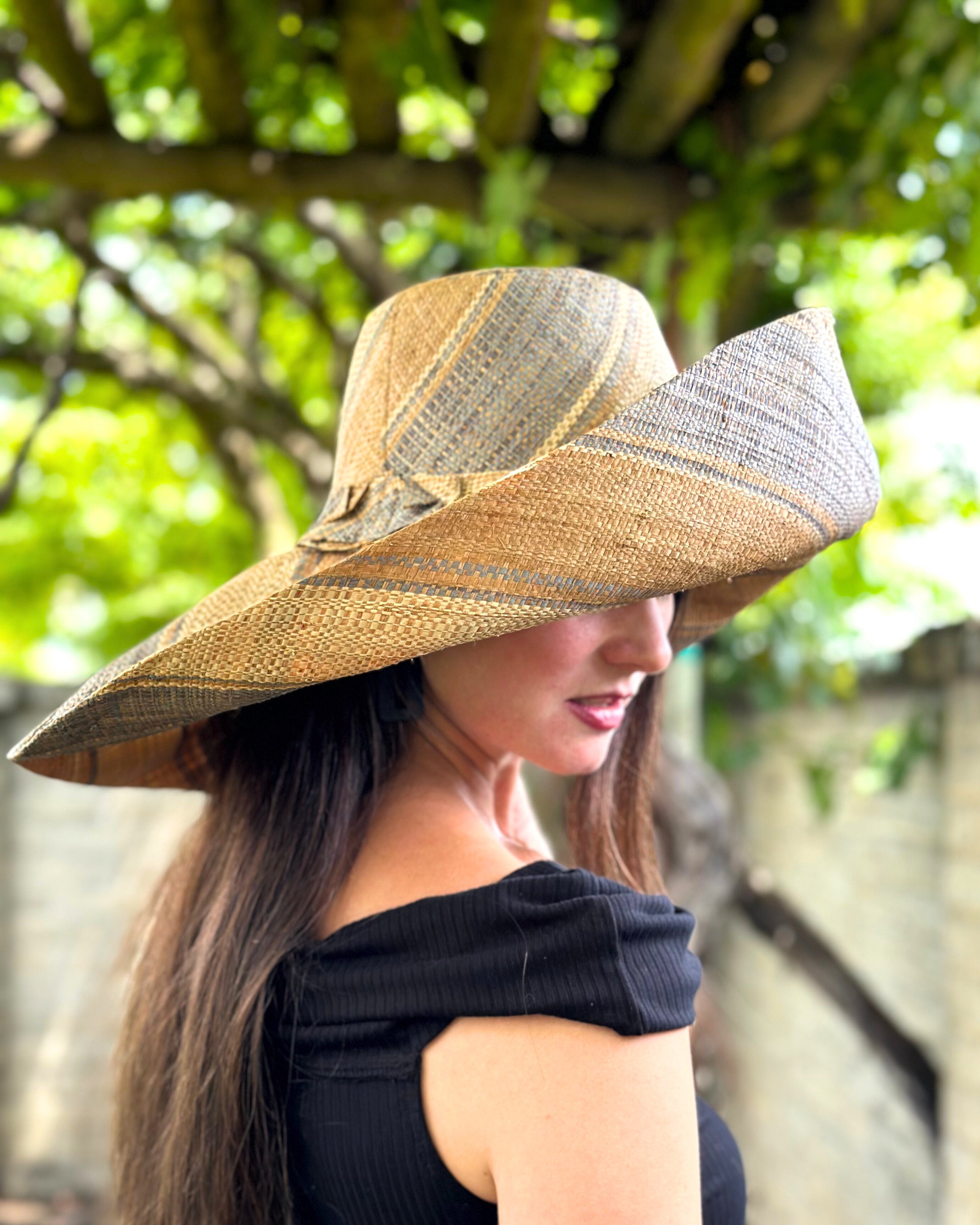 Model wearing Monica 7" Wide Brim Latte Swirl Multicolor Stripes Packable Straw Sun Hat Handmade loomed raffia in multi width bands of latte/light brown, grey, and natural create a swirl pattern - Shebobo