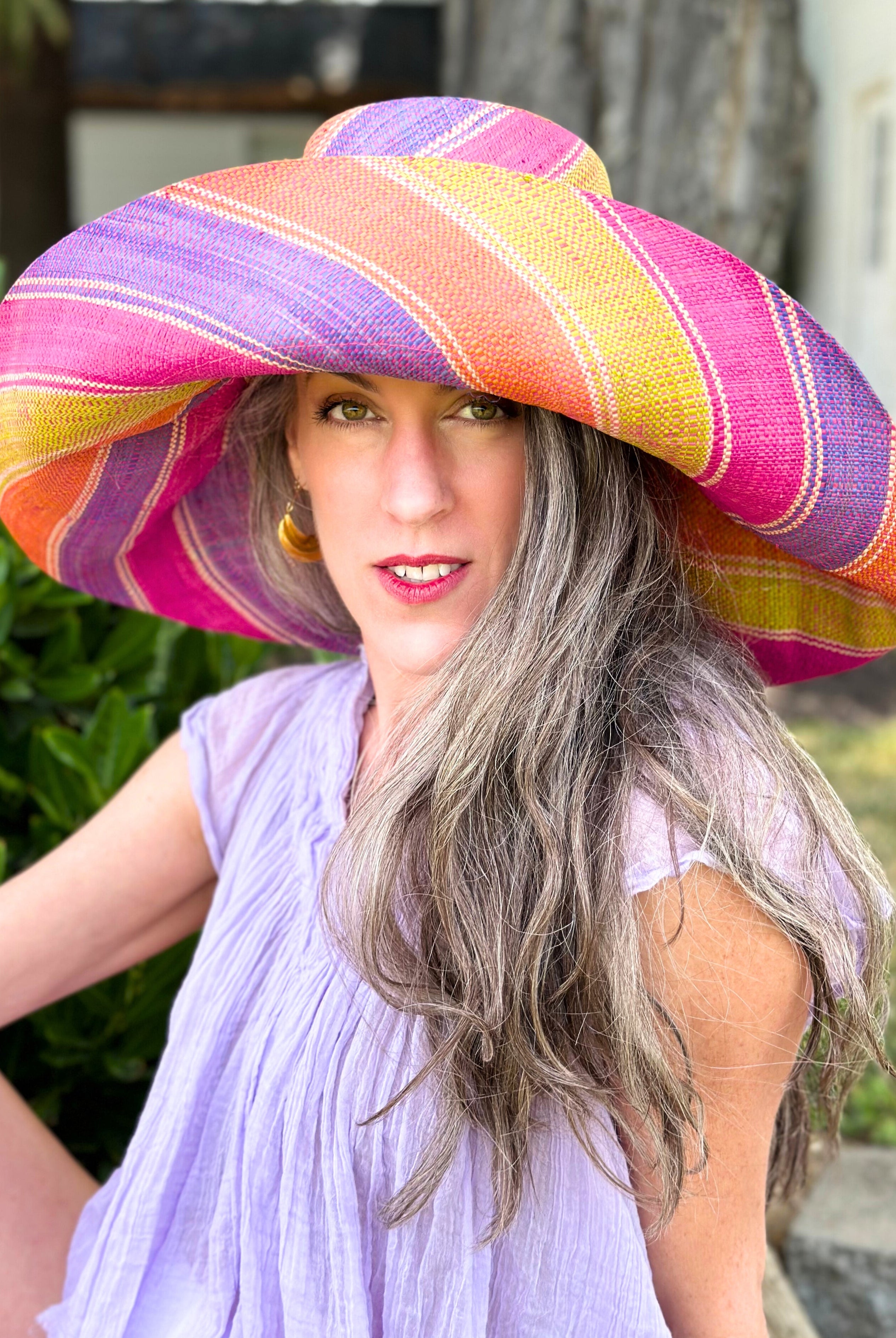 Model wearing Monica 7" Wide Brim Midori Swirl Multicolor Stripes Packable Straw Sun Hat Handmade loomed raffia in multi width bands of orange, lime green, fuchsia pink, purple, etc. create a swirl pattern - Shebobo