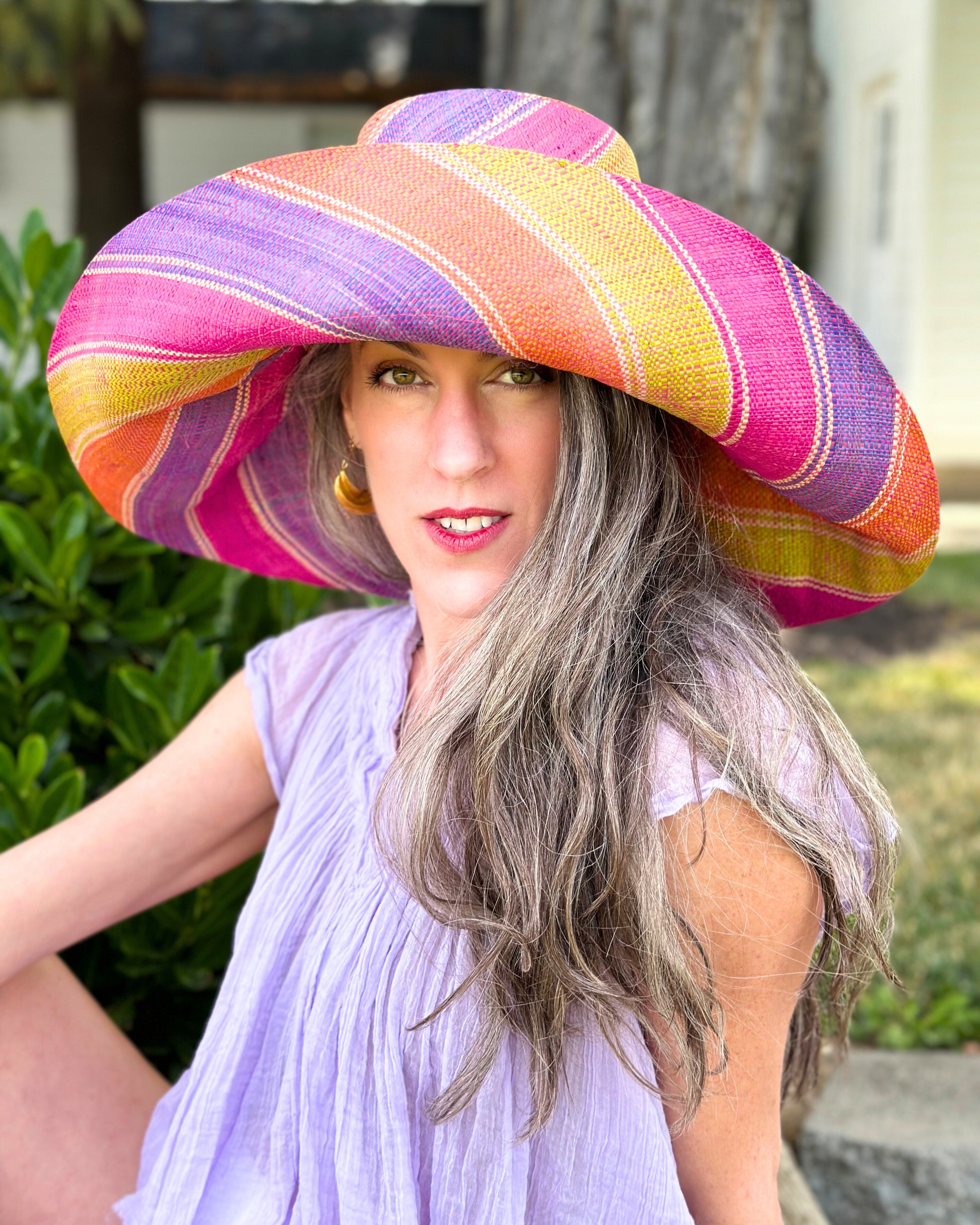 Model wearing Monica 7" Wide Brim Midori Swirl Multicolor Stripes Packable Straw Sun Hat Handmade loomed raffia in multi width bands of orange, lime green, fuchsia pink, purple, etc. create a swirl pattern - Shebobo