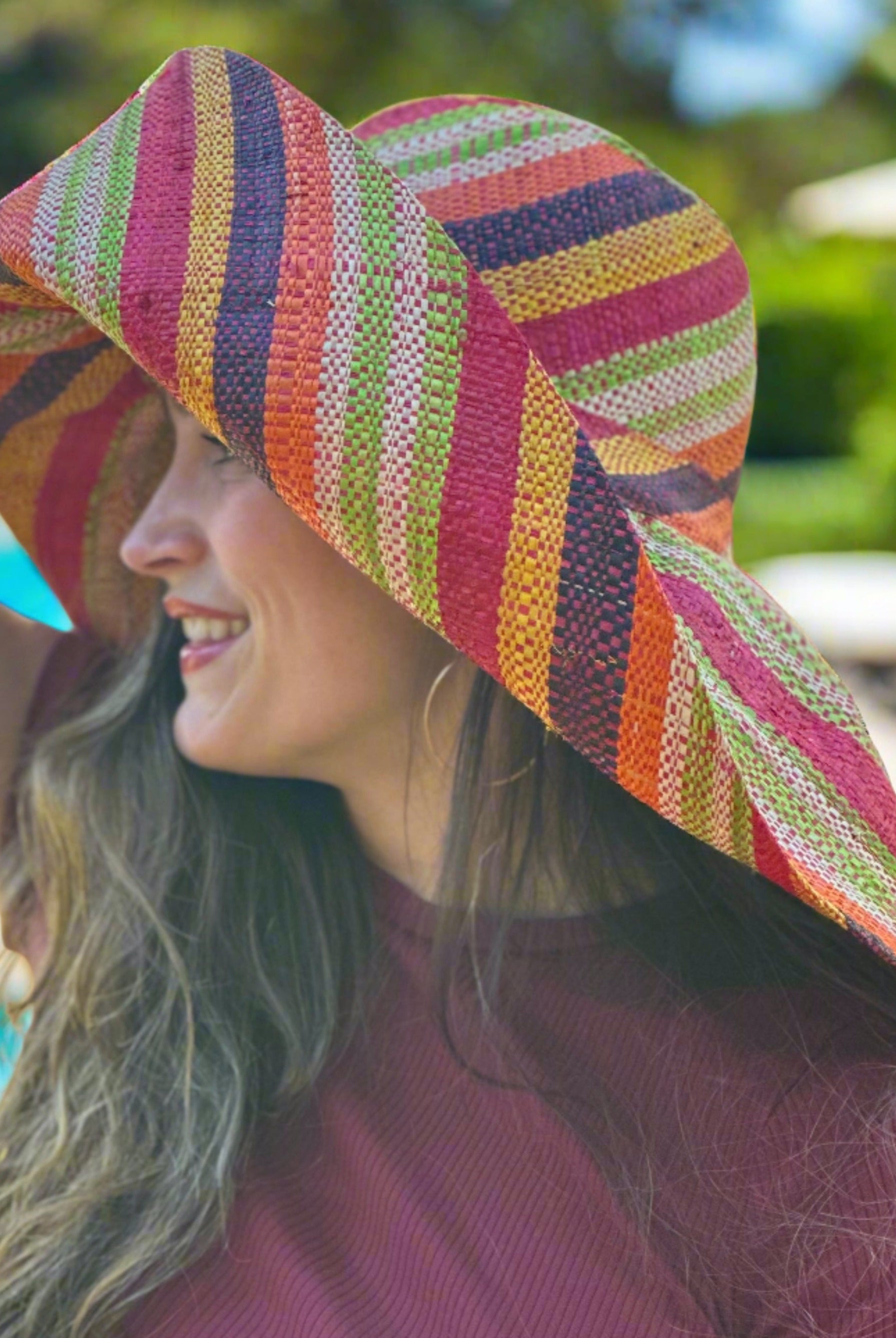 Model wearing Monica 7" Wide Brim Orange Stripe Multicolor Stripes Packable Straw Sun Hat Handmade loomed raffia multi width bands of orange, yellow, red, black, lime green, and natural straw color create a swirl pattern - Shebobo