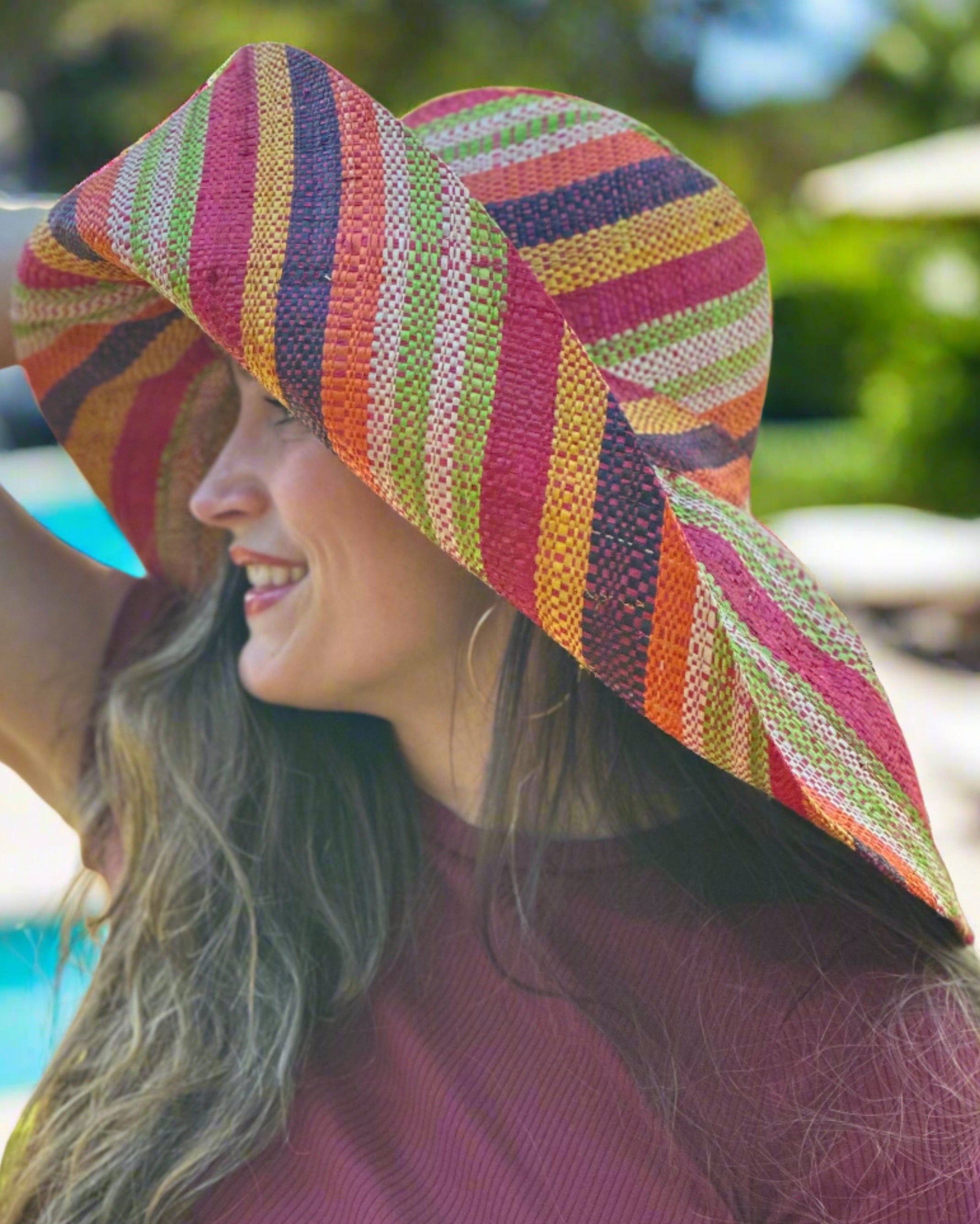 Model wearing Monica 7" Wide Brim Orange Stripe Multicolor Stripes Packable Straw Sun Hat Handmade loomed raffia multi width bands of orange, yellow, red, black, lime green, and natural straw color create a swirl pattern - Shebobo