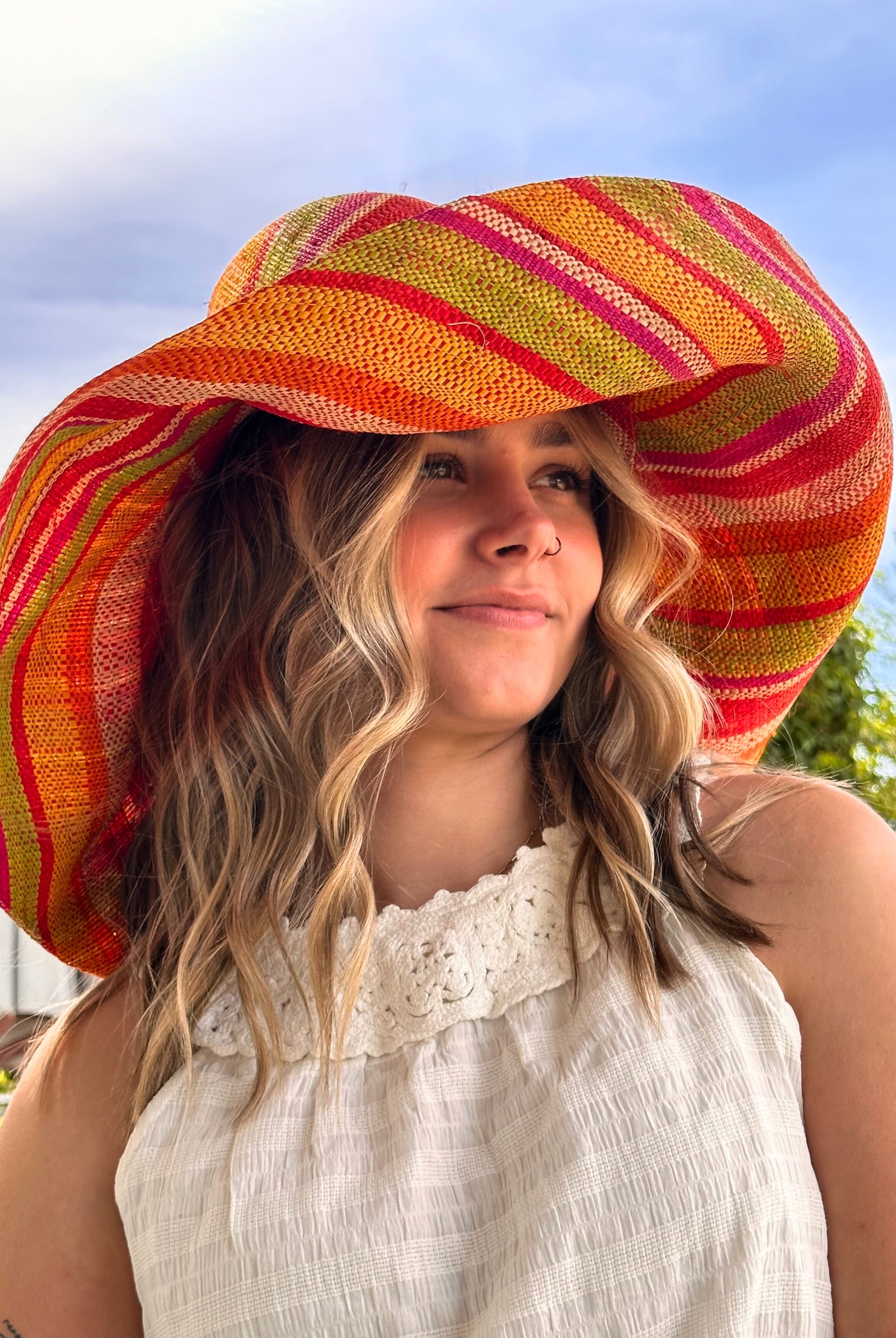 Model wearing Monica 7" Wide Brim Sunrise Stripe Multicolor Stripes Packable Straw Sun Hat Handmade loomed raffia in multi width bands of saffron yellow, fuchsia pink, orange, red, lime green, and natural create a swirl pattern - Shebobo