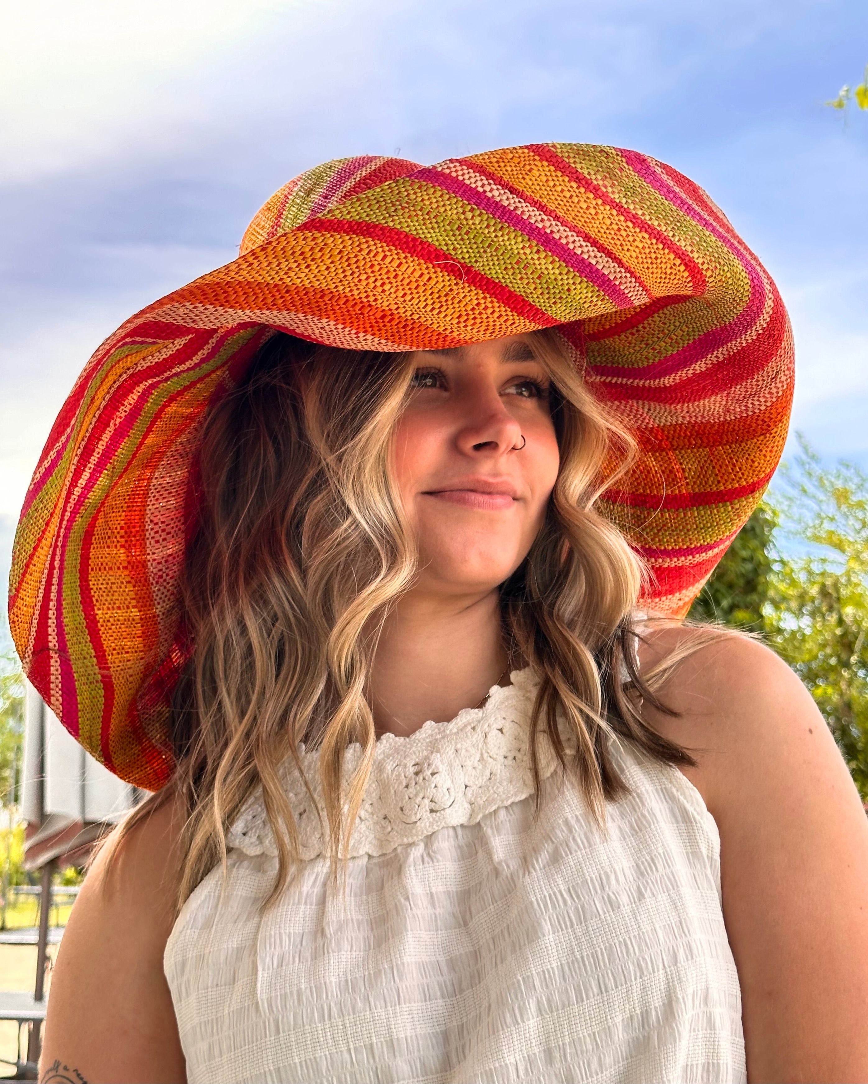 Model wearing Monica 7" Wide Brim Sunrise Stripe Multicolor Stripes Packable Straw Sun Hat Handmade loomed raffia in multi width bands of saffron yellow, fuchsia pink, orange, red, lime green, and natural create a swirl pattern - Shebobo