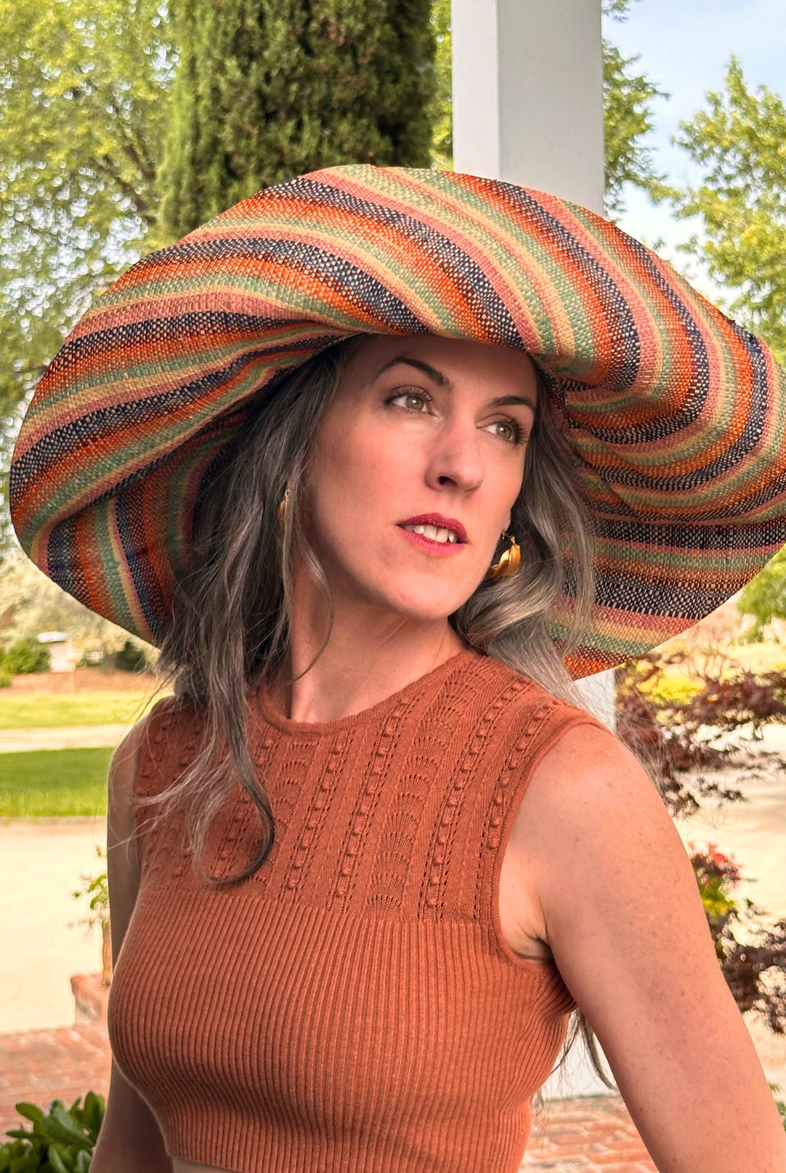 Model wearing 5Monica 7" Wide Brim Taffy Multicolor Stripes Packable Straw Sun Hat Handmade loomed raffia in multi width bands of saffron yellow, turquoise blue, seafoam blue/green, orange, pink, bordeaux red, etc., and natural create a swirl pattern - Shebobo